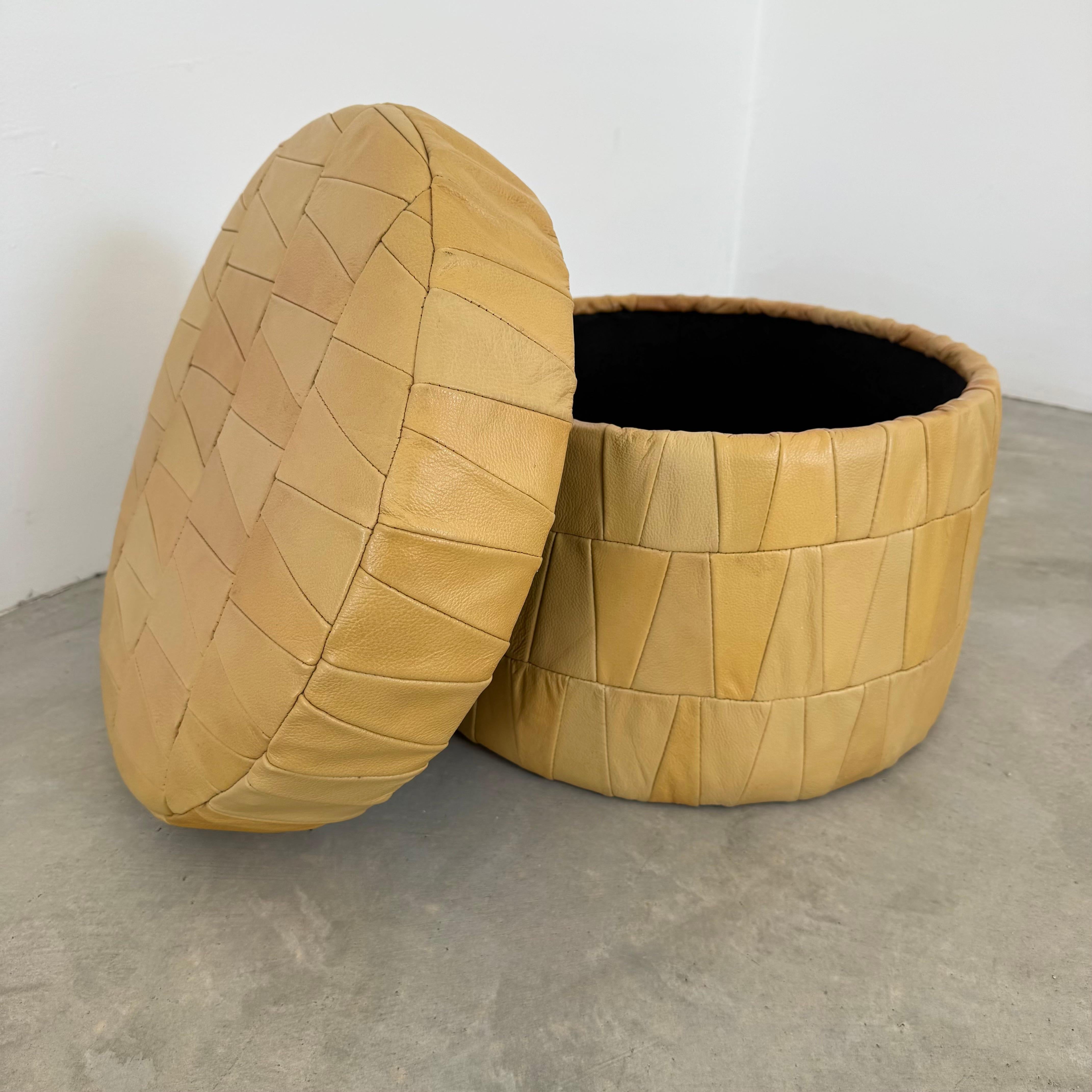 Una otomana cilíndrica de De Sede, con una rica textura, fabricada en Suiza en la década de 1970. Tapizada en el característico cuero patchwork, esta pieza muestra una gama de tonos arena y siena dispuestos en un mosaico geométrico de paneles de