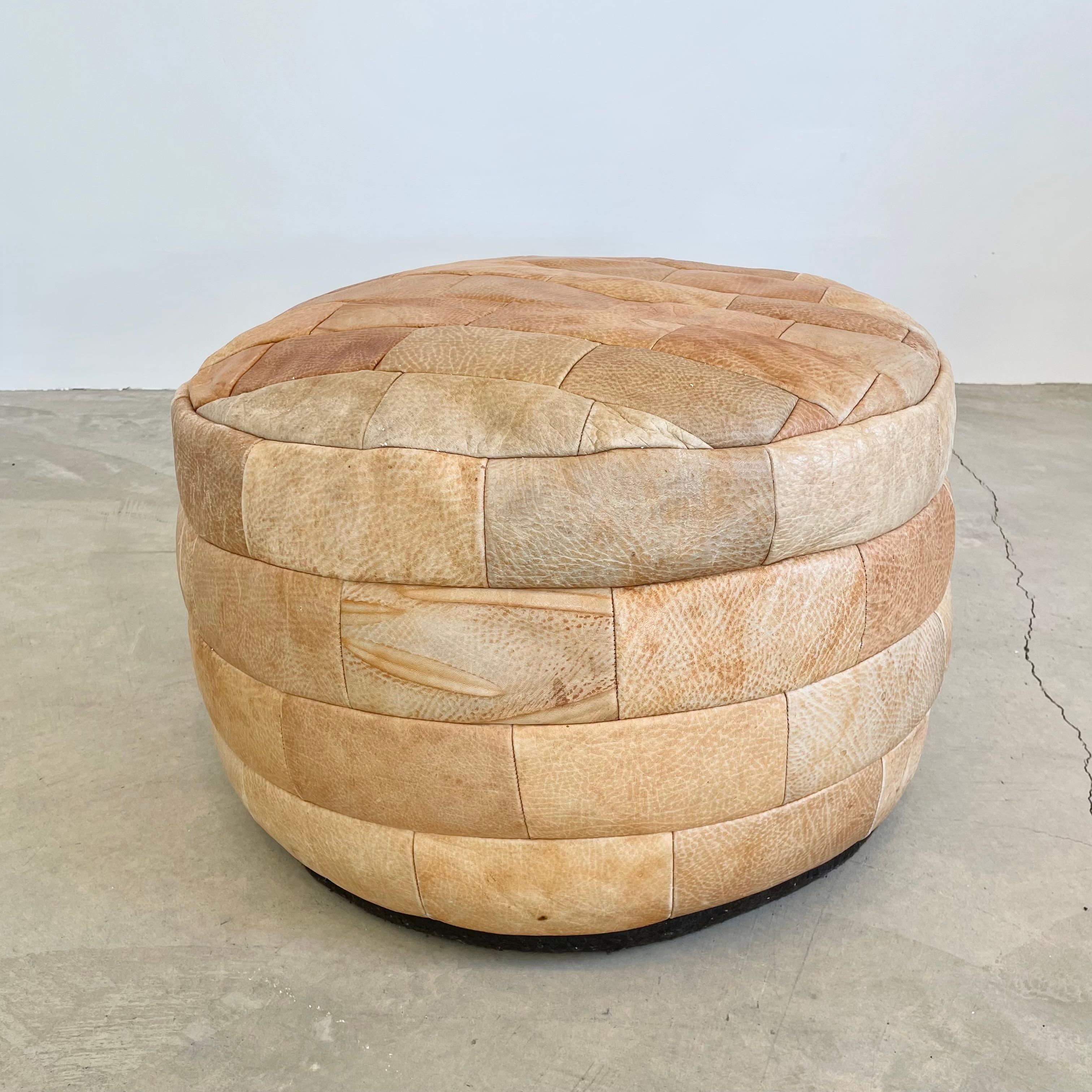 Wonderful tan colored leather pouf/ottoman by Swiss designer De Sede with square patchwork. Wonderful faded patina of varying degrees of tan, beige and brown. Perfect accent piece. Good vintage condition. Brand new filler. Perfect living room decor,