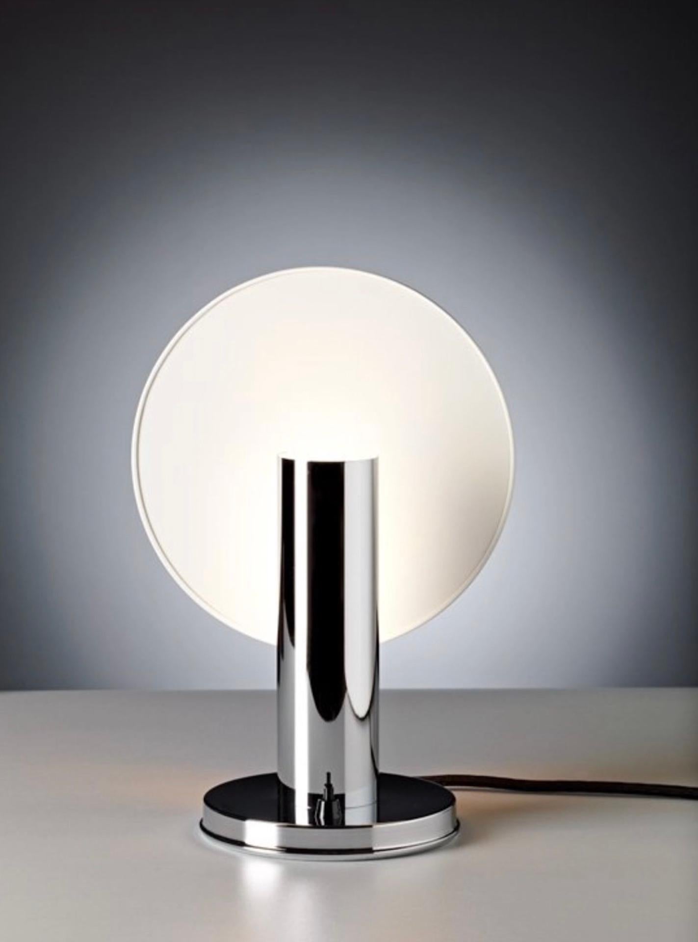 The light source for this bedside lamp is concealed in a cylinder that stands on a round baseplate, and the glow is reflected softly by a white varnished pane. The reflector screen is mounted asymmetrically and can be adjusted by simply turning it.