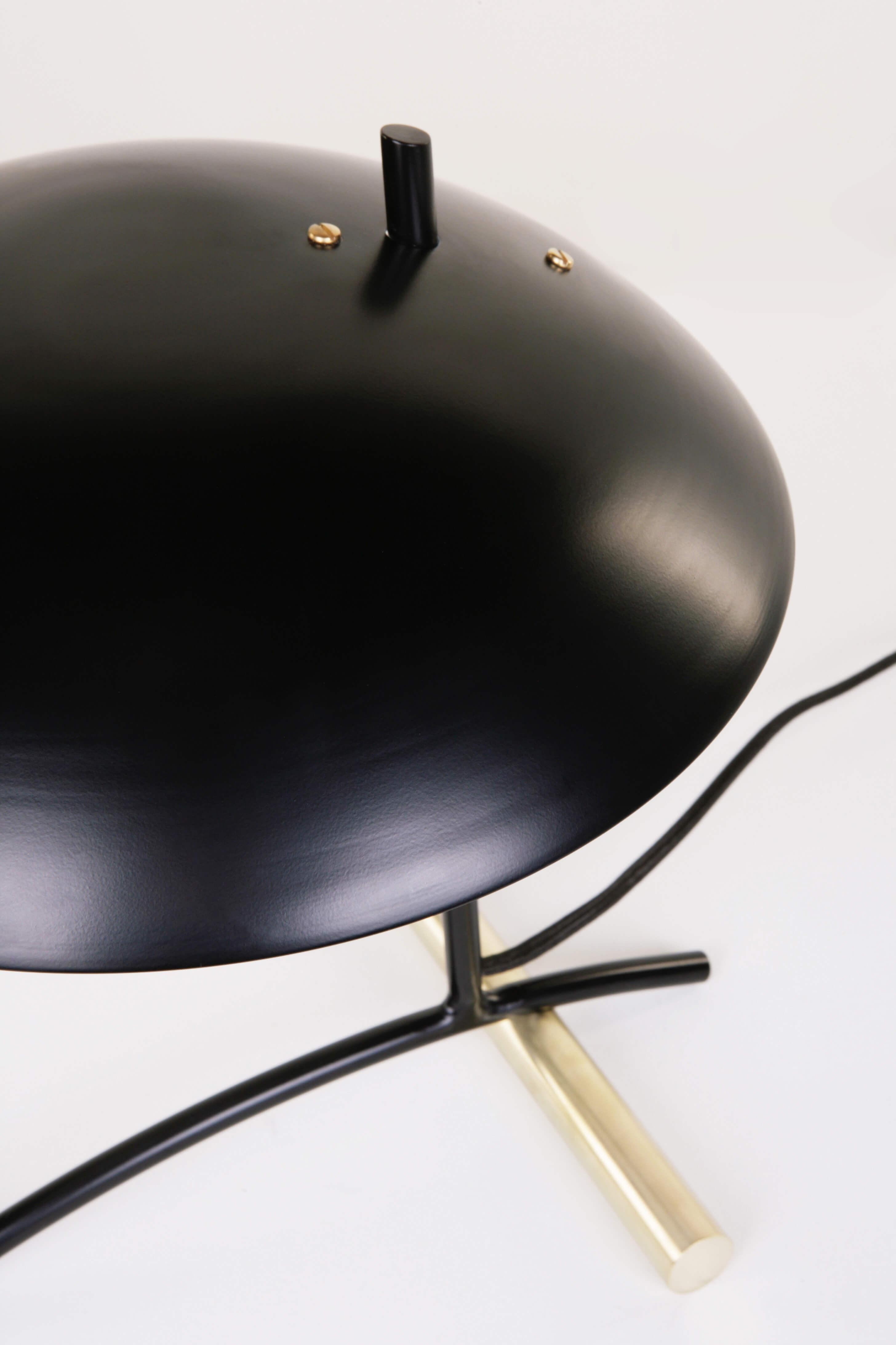La lampe de table , conçue par Dean Edmonds pour Atelier de Troupe , est composée d'une tige en acier et d'un poids tubulaire en acier massif ou en laiton pur , avec un abat-jour en aluminium . Les options de finition de l'abat-jour sont le noir ,