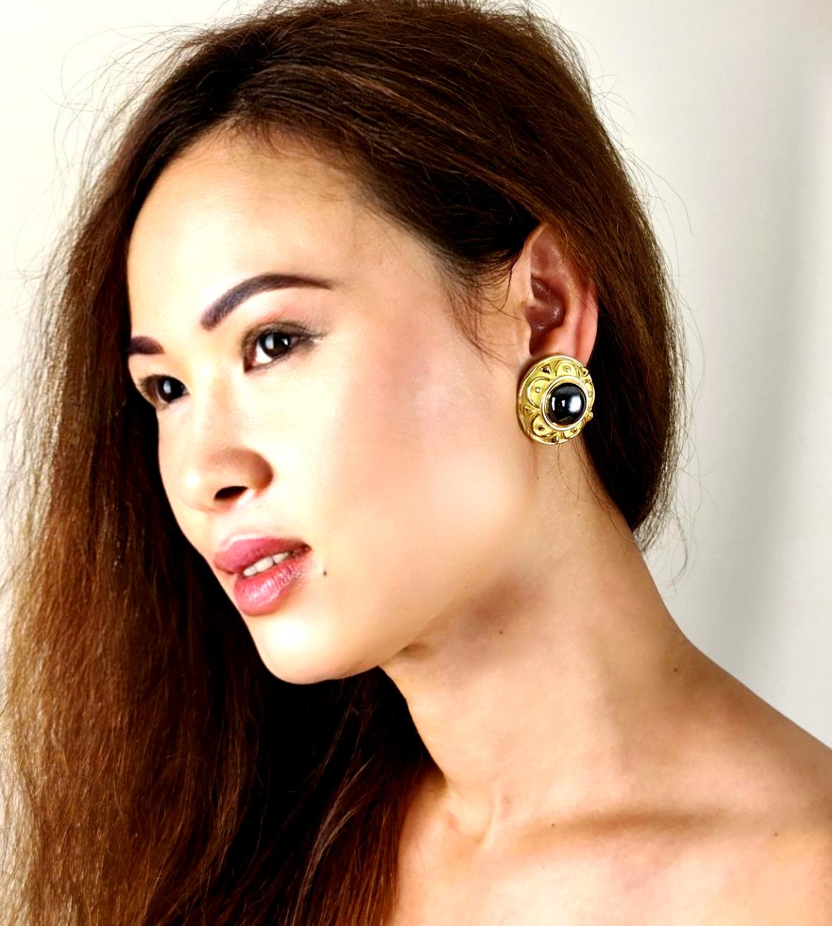 Beautiful pair of easy to access clip-on earrings by the legendary designer De Vroomen. The design consists a cabochon Hematite center and yellow gold dome with contrasts between a lighter shade of textured gold as the background and glistening