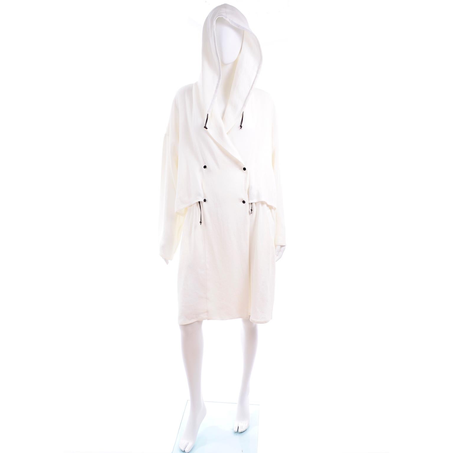 This is a gorgeous 100% linen drawstring hooded jacket from Dusan.  The coat is white with black drawstrings at the hood and waist. It crosses over to close with double breasted small black buttons. This luxe linen coat is deadstock with its