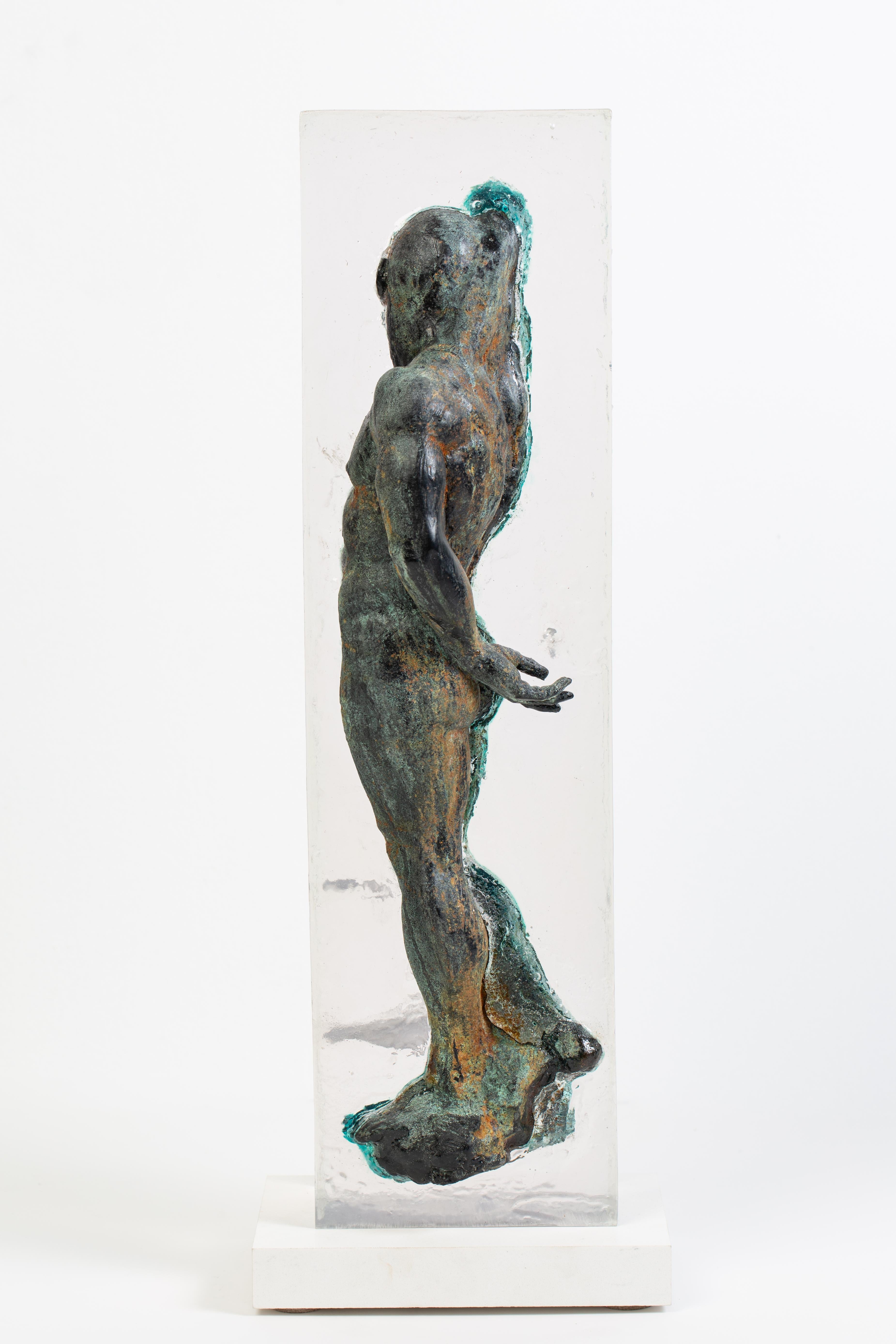 This unique and innovative sculpture of a figure half embedded in a clear resin block showcases the creative ways Dean Kugler chooses to approach sculpting.  The figure is finished in a green hue with flecks of brown rust to reference antique