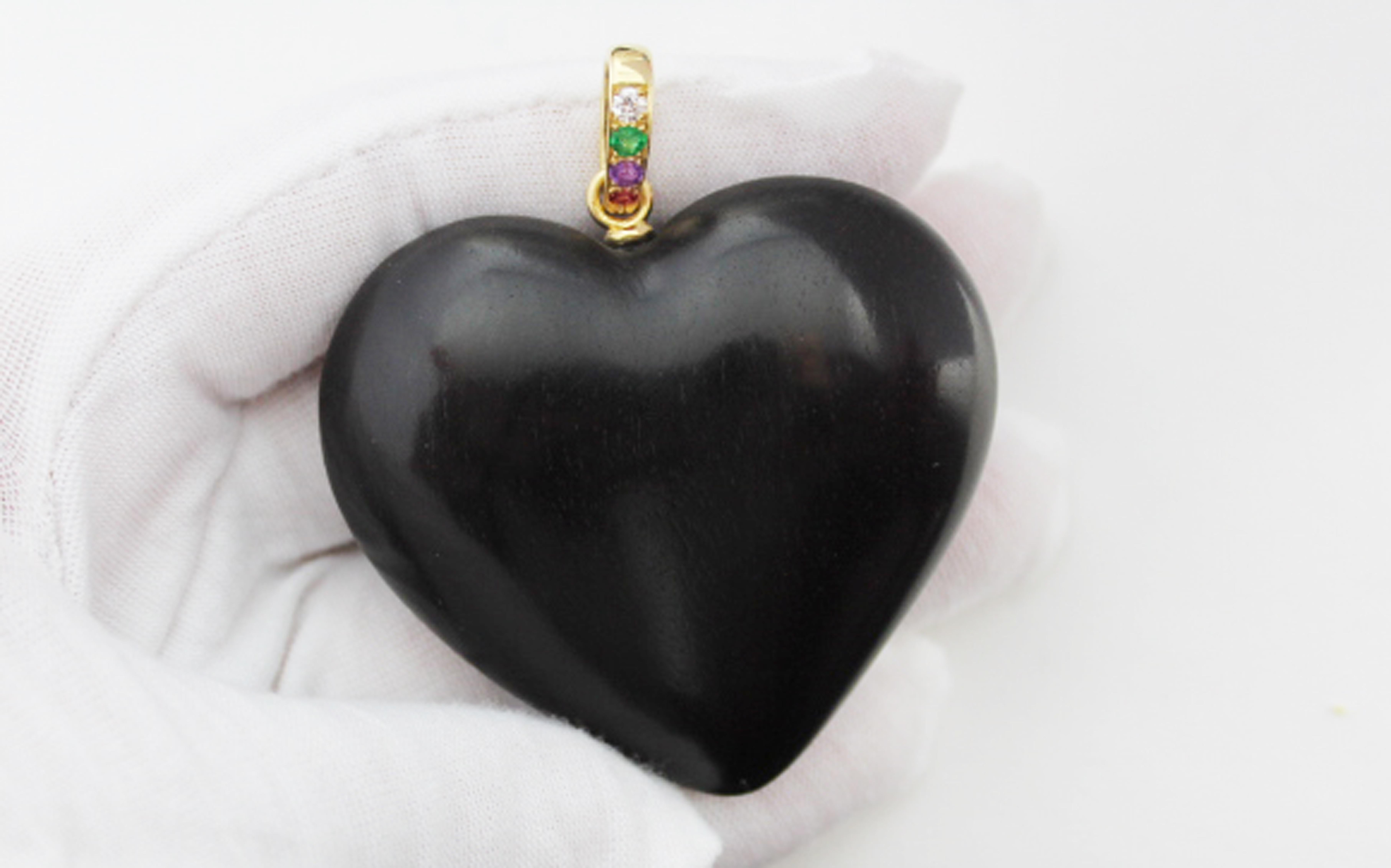 Hand carved pendant shaped as an heart made in ebony black wood.

On the claps:
-Diamond 
-Emerald 
-Amethyst 
-Ruby

The stones have been mounted in the order to recreate with the initial the stones the word : 
 DEAR.

Mounting in 18 karat yellow