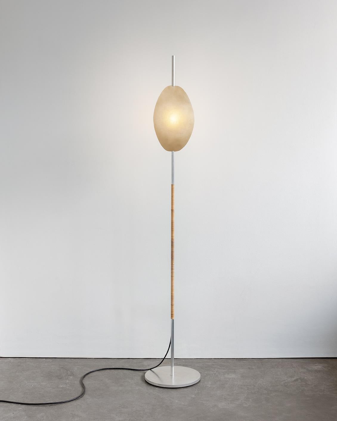 Deas Licht von Calen Knauf
Abmessungen: T 28 x B 28 x H 161 cm
MATERIALIEN: Aluminium, Rattan, Rohhaut, Harz

Die Deas ist eine Stehleuchte, die aus einem massiven, gewachsten Aluminiumsockel besteht, der von Hand mit Rattan umwickelt ist. Der