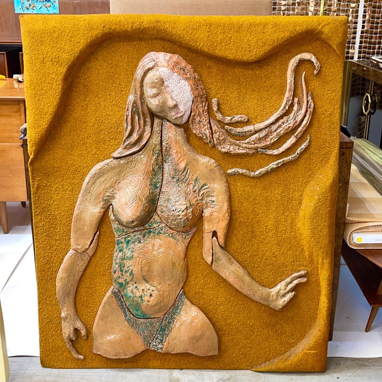 A modernist portrait of a semi-nude woman executed in segments of glazed ceramic mounted to a sculpted plywood panel clad in a coarsely woven textile in honey mustard color.
Signed en verso 