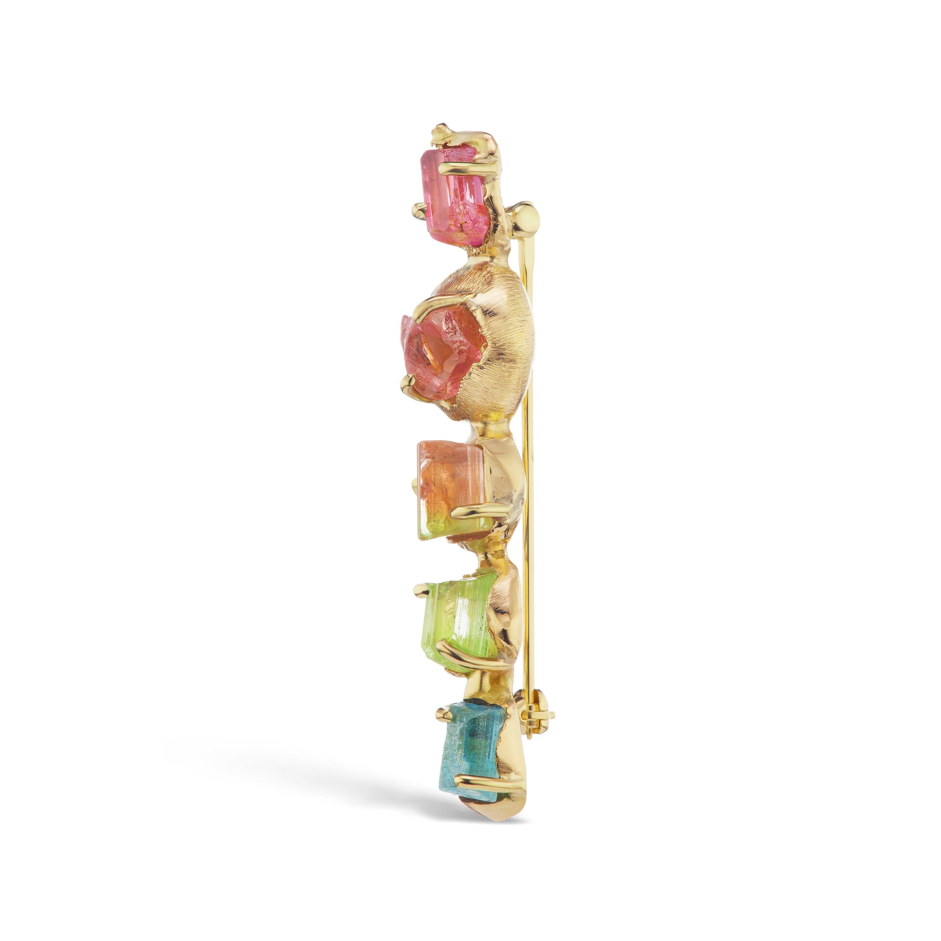 The one-of-a-kind Tsavo Sunphase lapel pin is hand-crafted in 18-karat recycled yellow gold, and showcases five untreated, Tenda Cut, natural color tourmaline in shades of pink, peach, green, and blue. The tourmalines are set in a linear row, in a