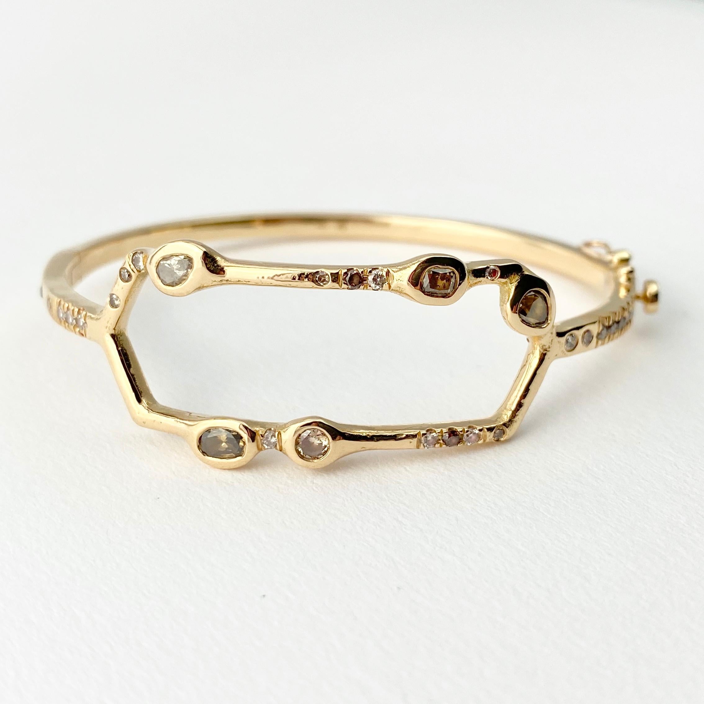 The Debra hinged bangle bracelet is hand-crafted with 18-karat recycled yellow gold, and features five bezel set, colored diamonds (two pear shape, one cushion, one oval, and one round); and 25 round champagne accent diamonds. The hidden box clasp