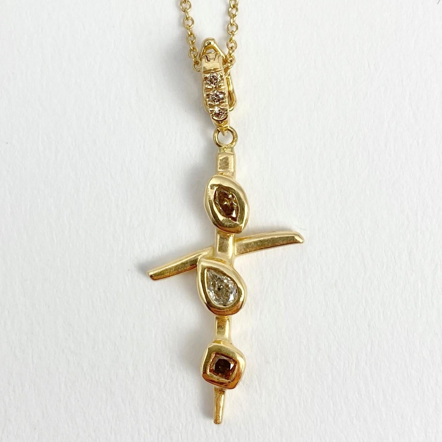 The Crossroads Cross pendant is hand-made with 18-karat recycled yellow gold, and features three bezel set, natural colored diamonds (one marquise shape, one pear, and one cushion); and three round brilliant, champagne accent diamonds set in the