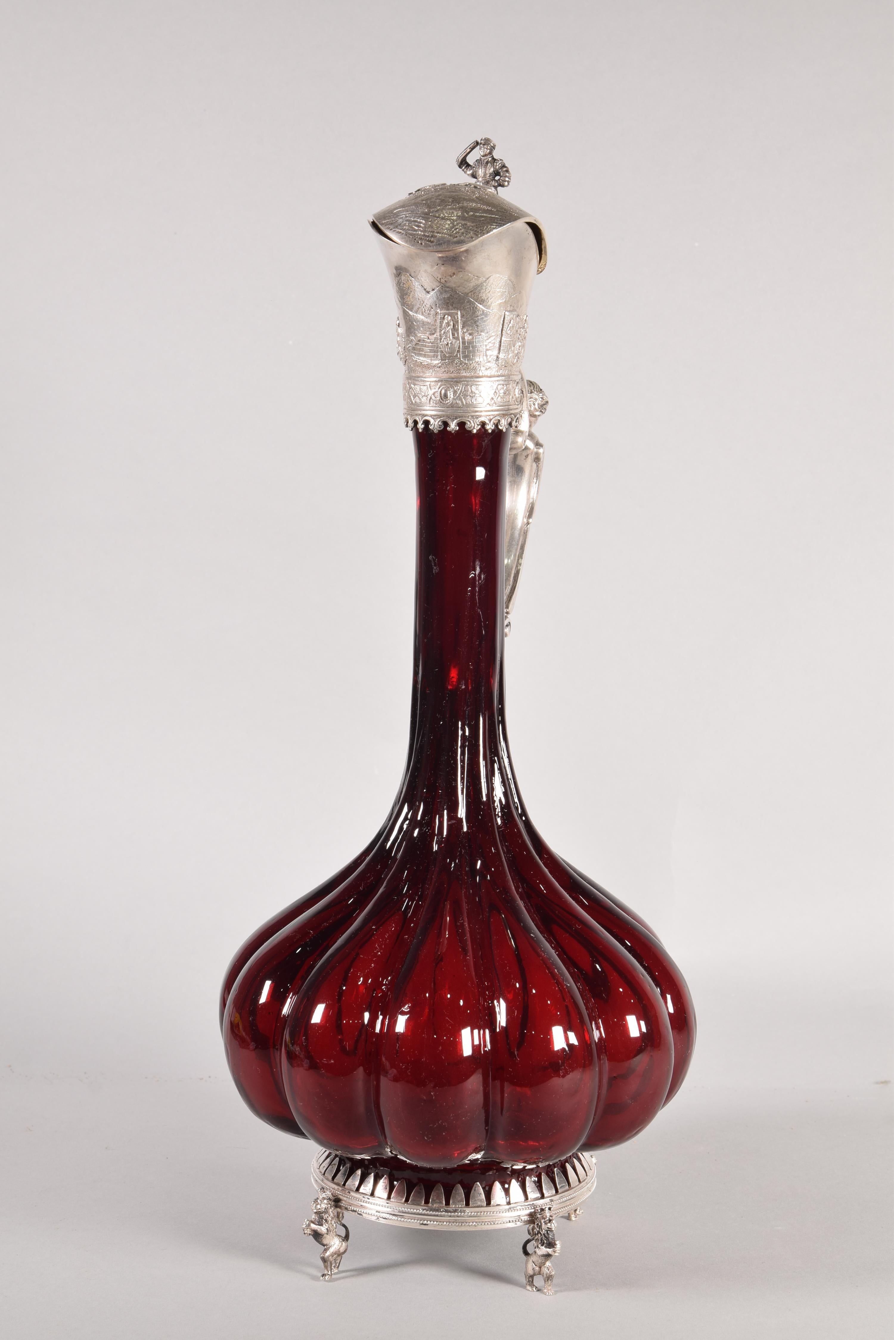 Jug. Garnet glass, silver frame. Possibly Germany, 19th century. 
 With contrast markings. 
 Jug with a dark red glass body and gallon shape, widening towards the base, and a silver frame in its color. It has a base supported by rampant lions, a