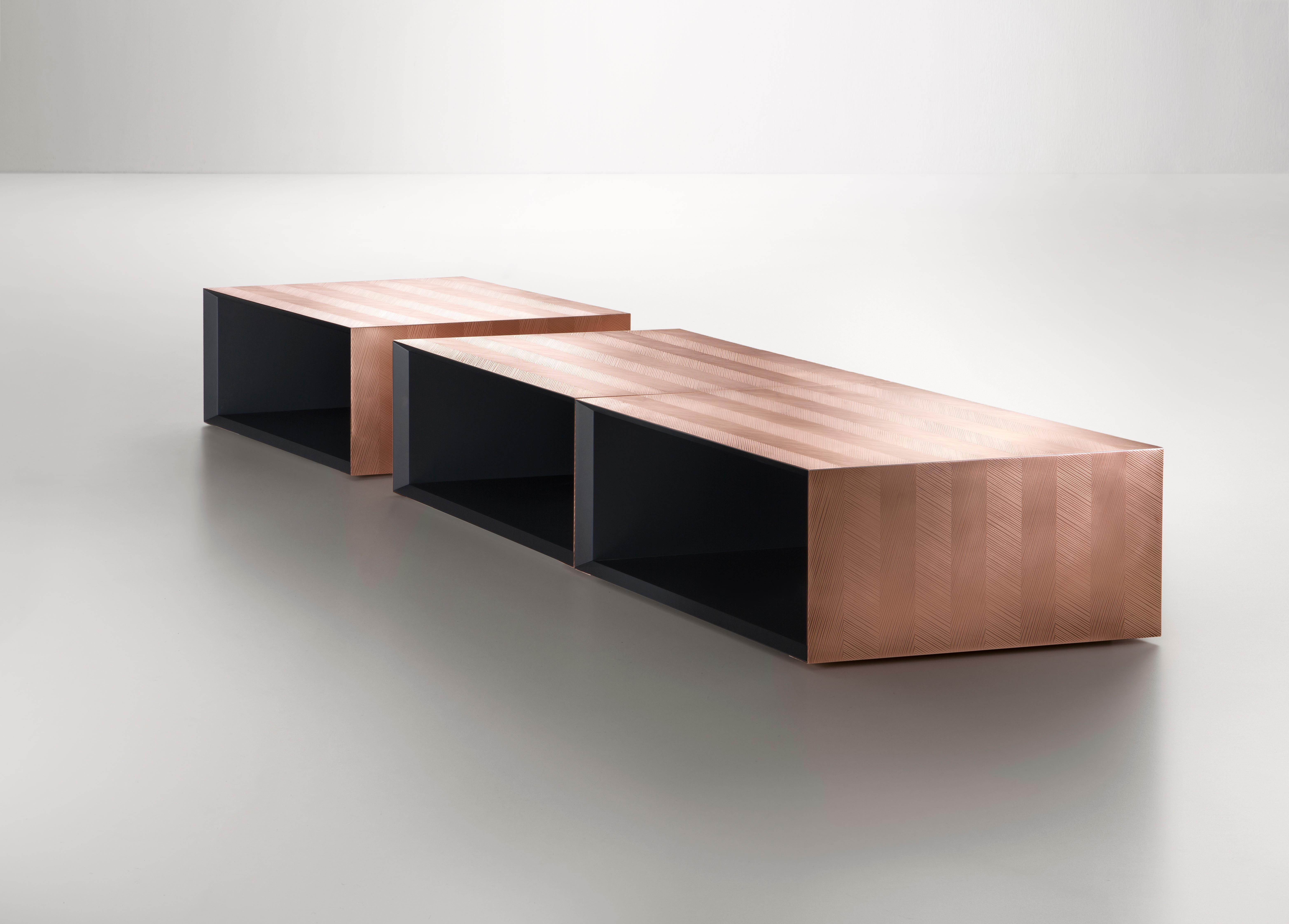 A small rhomboid-shaped table with storage space. Its simple shape renders it modular: by combining it with other identical elements, either moved around or rotated, numerous configurations can be obtained. The natural copper “skin” worked using the