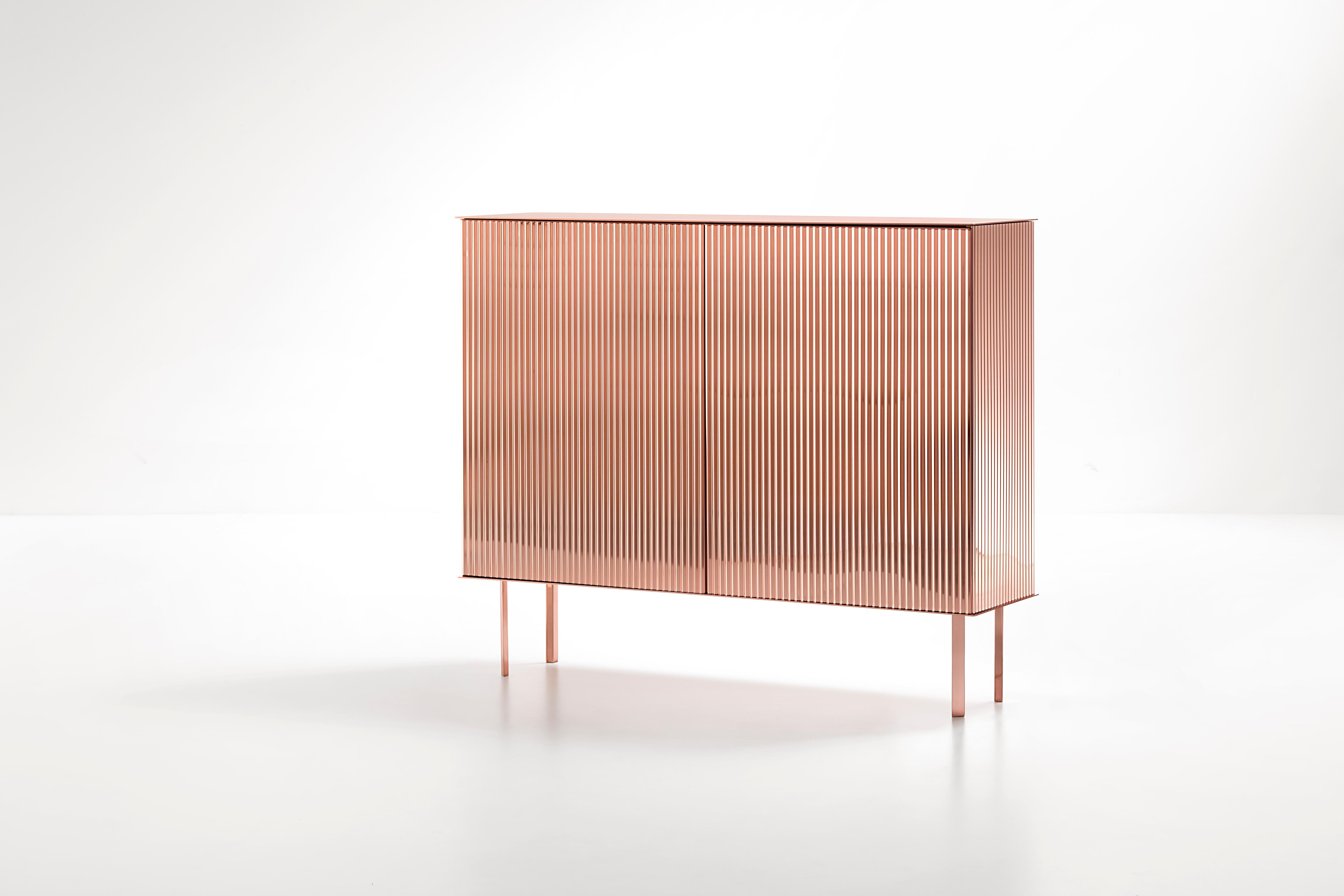 Like a ballerina on her toes, Elizabeth gracefully unfurls her luminous dress, as if made of pleated fabric. The characteristic folds add movement to the metal sheet along the surface of the cabinet, transforming each reflection into light. In an