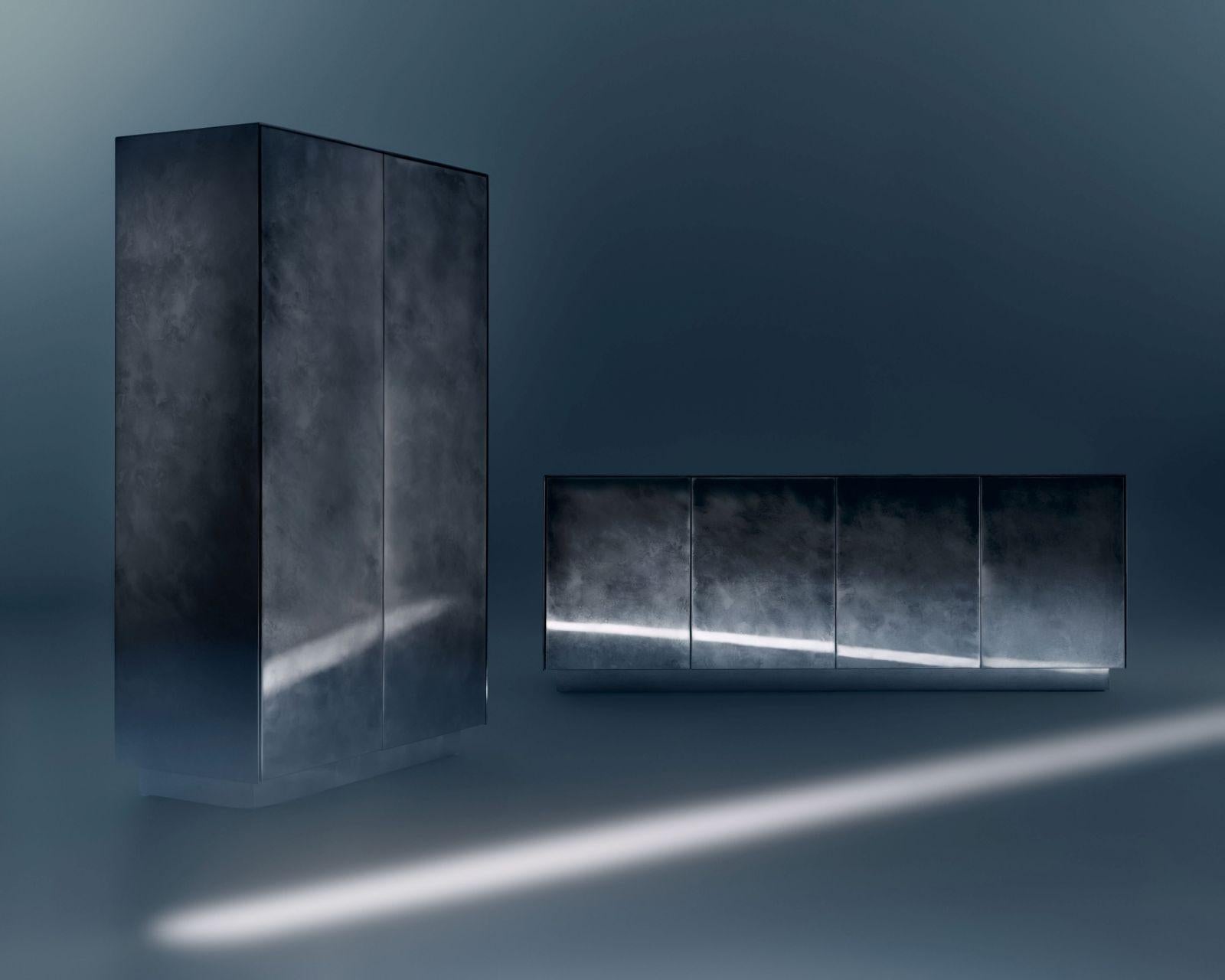 Le tracce del tempo sono disegnate una sopra l'altra, infuse nella pelle mutevole delle rigorose forme metalliche che definiscono questi mobili. L'armadio si estende in verticale, con due ante che si aprono dando spazio ad ampi ripiani e