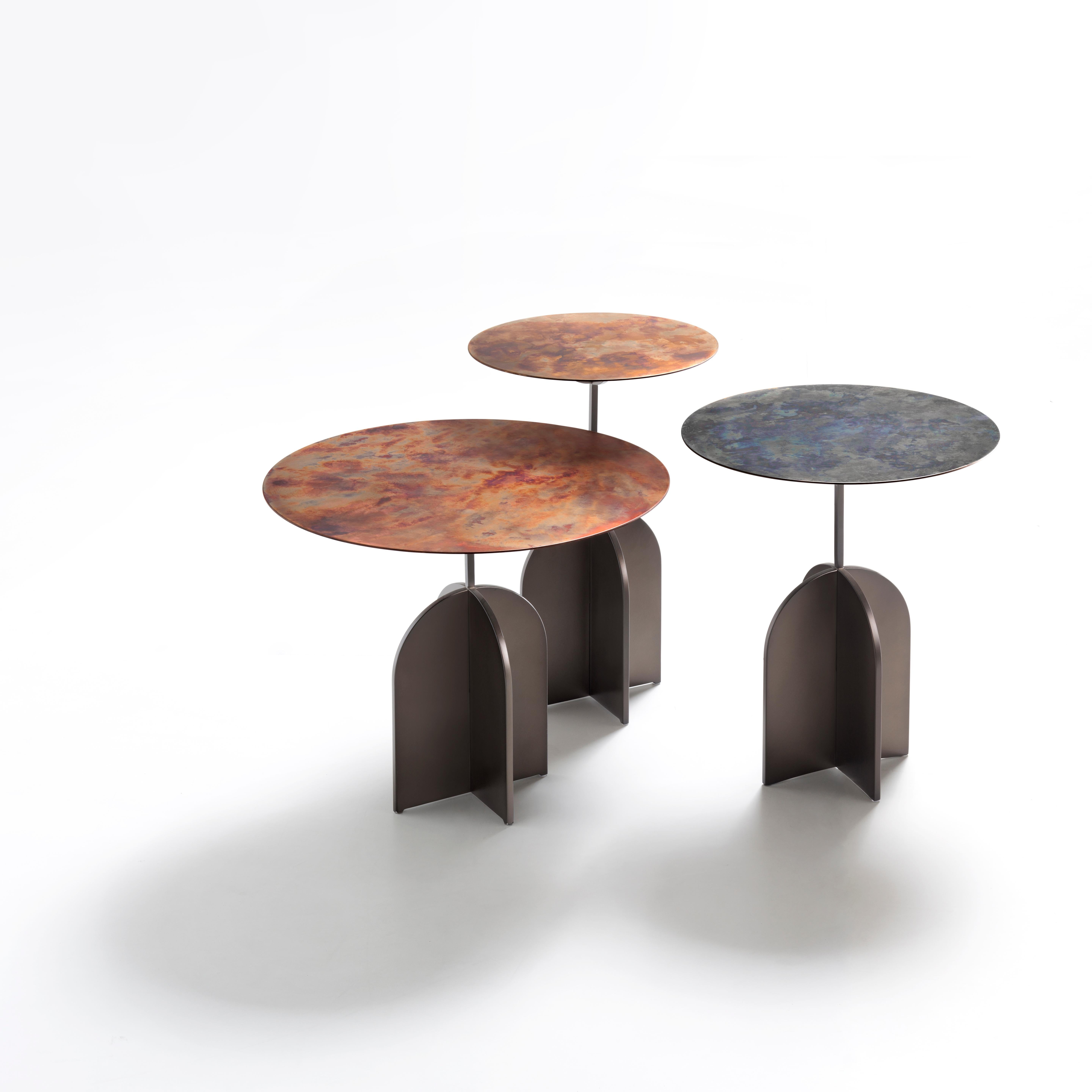 Decisive geometries for a table characterized by the superimposition of three apparently-contrasting elements. The robust cross-shaped base anchors the structure to the ground while the thin round top rests on a slender stem, like a delicate leaf