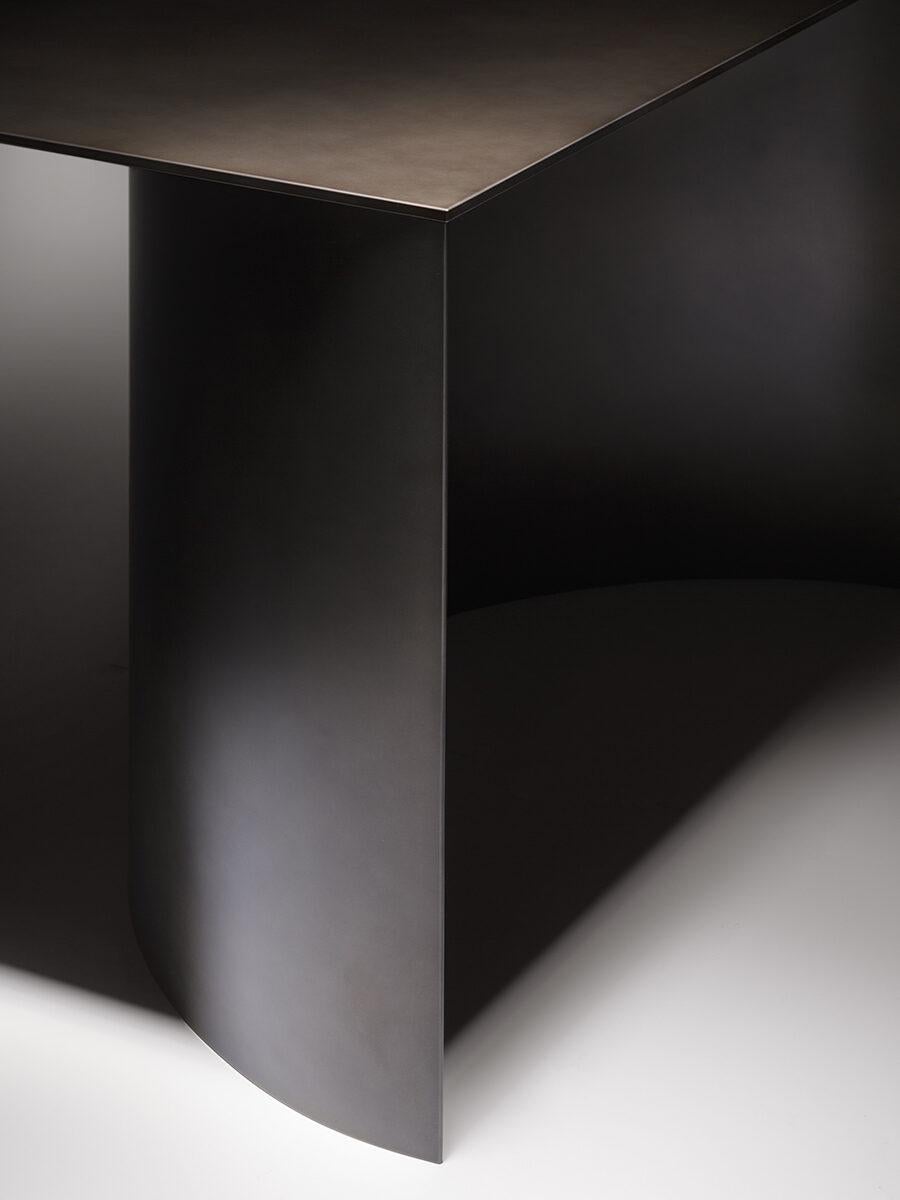 Une présence sculpturale et un minimalisme essentiel sont les caractéristiques de cette table, composée de trois éléments seulement : un épais plateau rectangulaire qui repose sur deux grands demi-cylindres concaves, créant ainsi un piédestal. Les