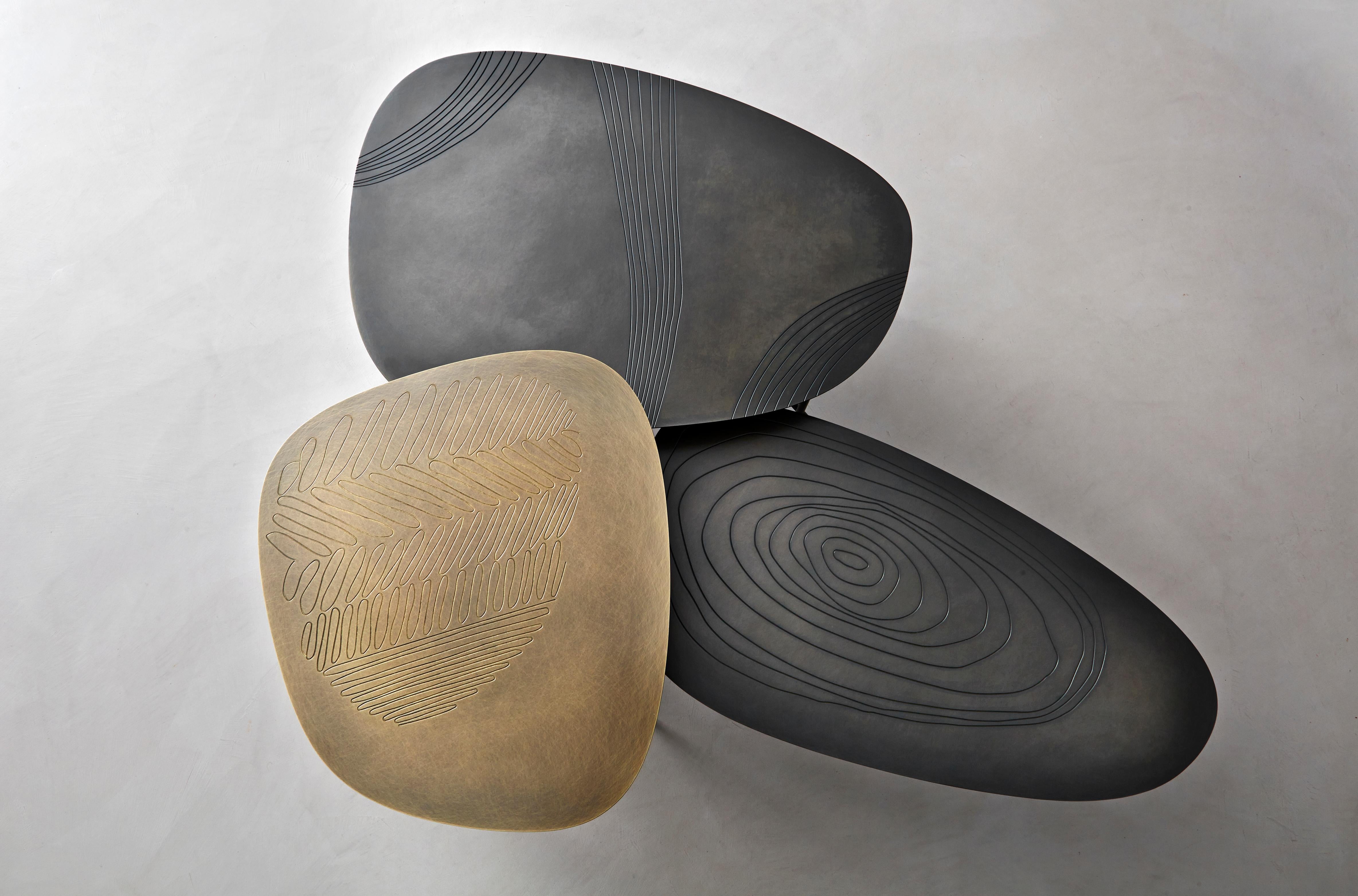 In organic shapes, this triptych of small tables is supported by a slender rebar structure and characterized by geometric shapes etched on metal tops. Flowing forms, almost primitive markings, material combinations and chromatic variations combine: