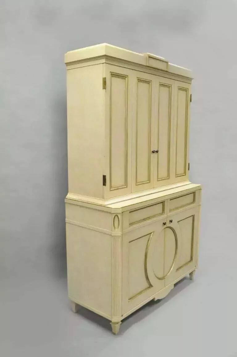 Mobile bar francese neoclassico in stile Luigi XVI dipinto in crema e oro di Decca (A). L'articolo presenta una struttura pesante in due parti con finitura crema dipinta a fuoco e finiture dorate. Il mobile è inoltre dotato di due ante superiori con