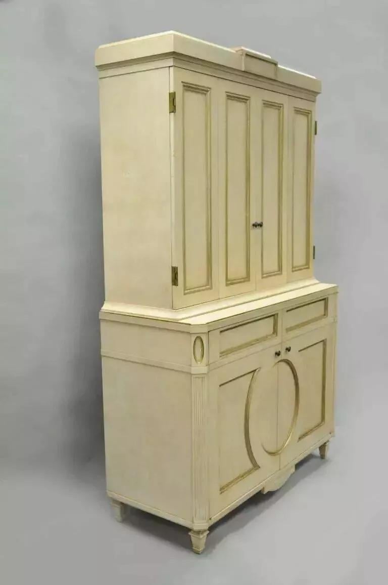 Mobile bar francese neoclassico in stile Luigi XVI dipinto in crema e oro di Decca (B). L'articolo presenta una struttura pesante in due parti con finitura crema dipinta a fuoco e finiture dorate. Il mobile è inoltre dotato di due ante superiori con