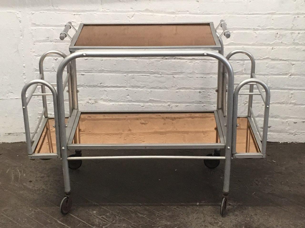 Deco bar cart / service trolley with removable tray has a brushed aluminum frame, peach mirrored glass tops, three bottle holders on each side, and four wheels for easy moving.