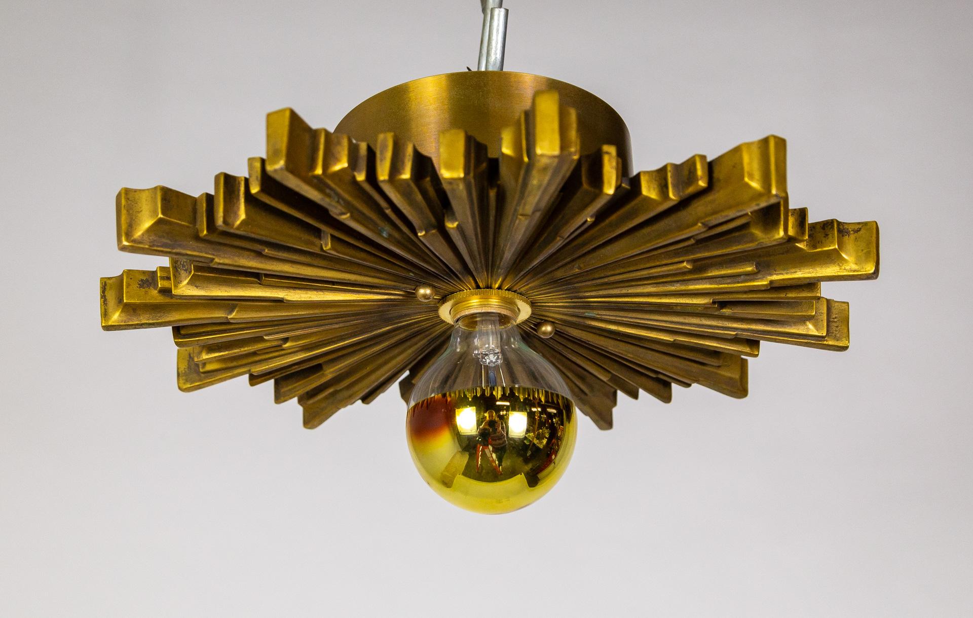 A finely cast metal starburst light fixture in deep gold tone from the early 20th century. The radial shape mimics sun beams in Art Deco style. Newly rewired with a high relief mount so it floats off the ceiling adding depth to the design.  14