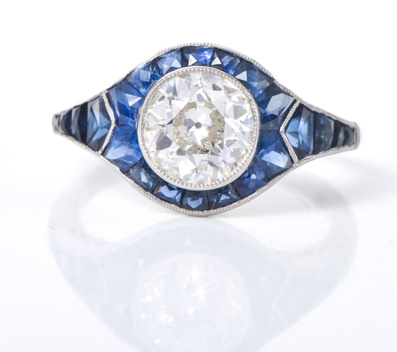 Affascinante e vivace, questo anello di fidanzamento Deco Design in platino presenta un diamante rotondo di 1,27 carati con taglio antico, colore G-H e purezza SI, incastonato al centro.

È circondato da 1,20 carati di zaffiri blu naturali calibrati