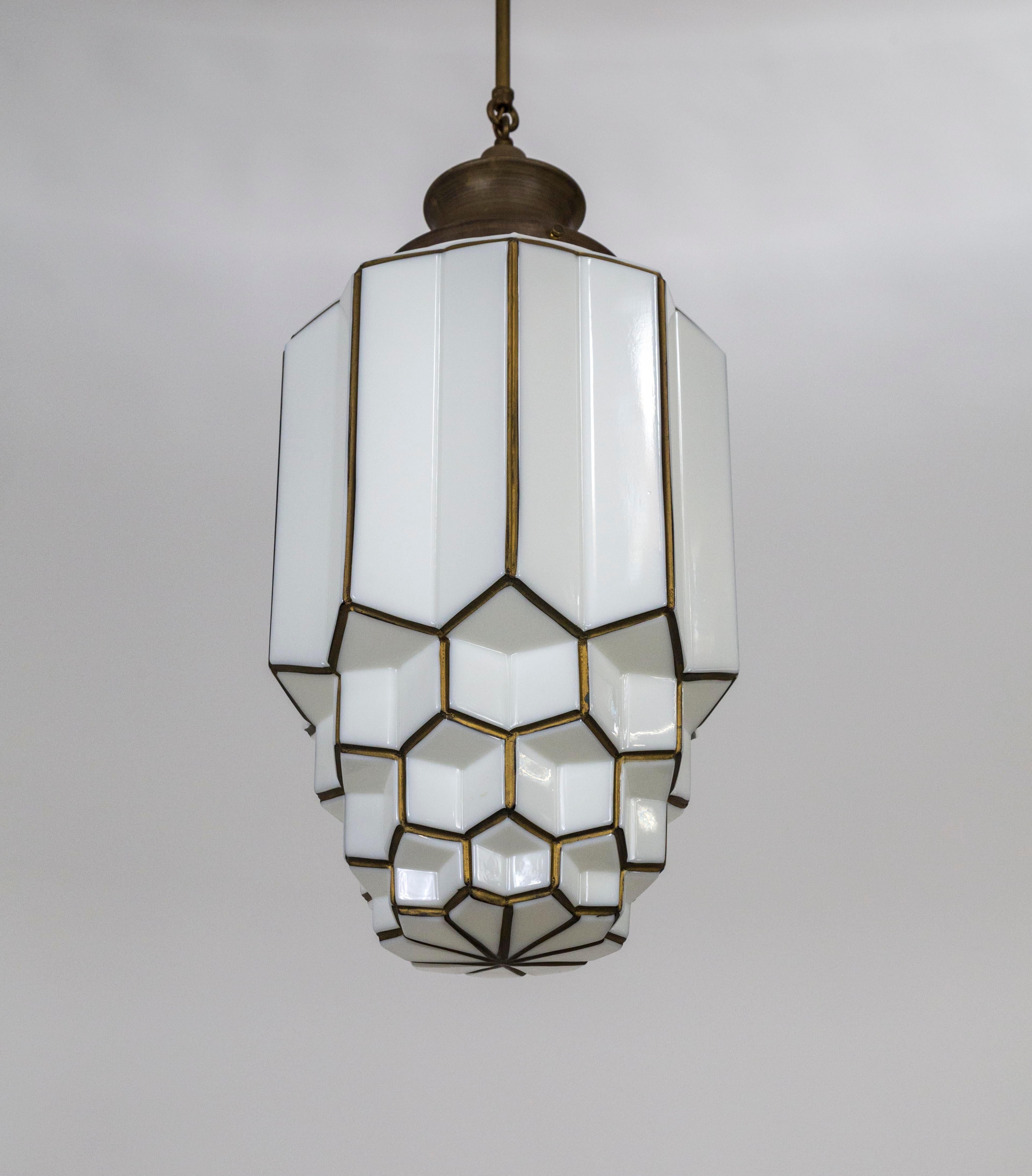 A multifaceted, cylindrical, white molded glass, skyscraper style pendant, outlined in antique gold paint. The complex, stepped form creates the look of honeycomb and star shapes, and even a lotus flower from directly below. A bold and elegant Art
