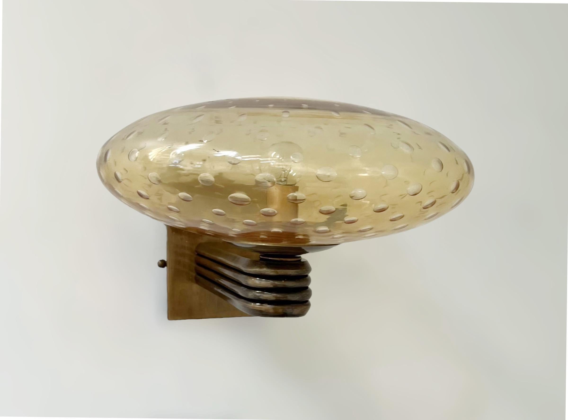 Aplique de pared italiano de estilo Art Decó con pantalla de cristal de Murano ámbar soplado a mano con burbujas en el interior del cristal mediante la técnica de Bollicine, montado en marco de acabado bronceado / Diseñado por Fabio Bergomi para