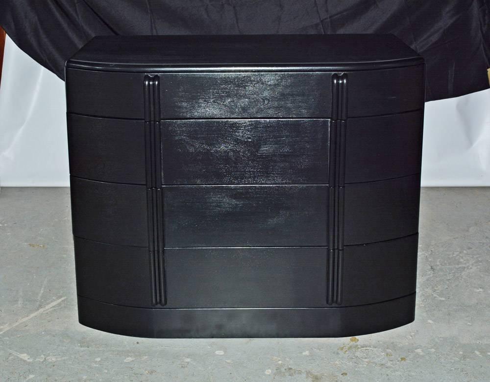 Painted glossy black, the moderne chest of drawers has a three-sectioned drawer at the top and three deep drawers below. The side boards of each drawer are set in the grooved curved front panels while the back edges of the side boards are dovetailed