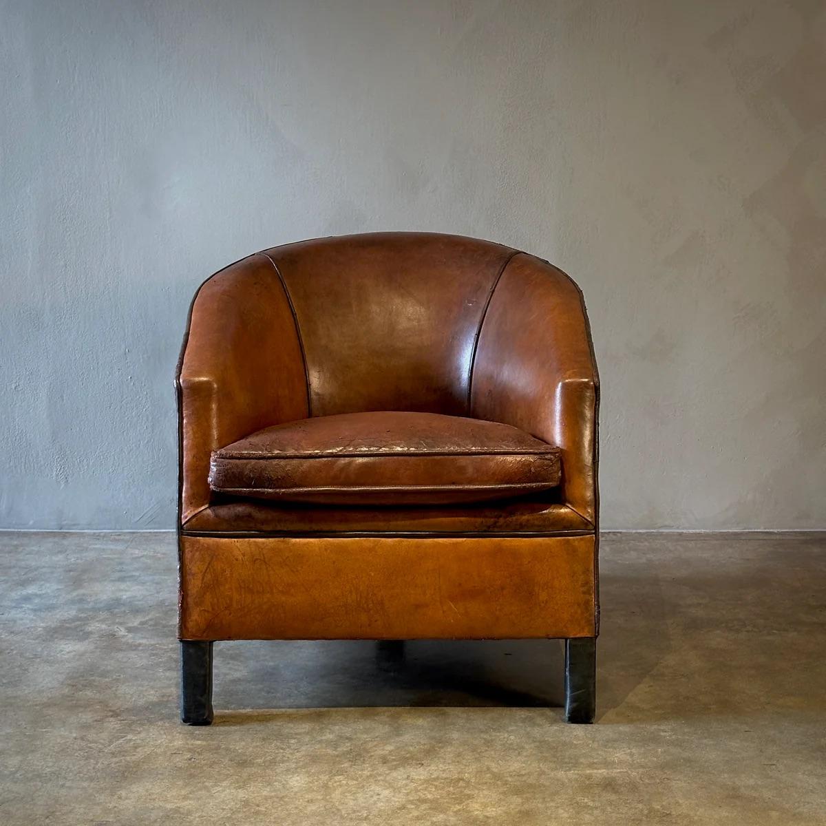 This refined French Art Deco armchair, upholstered in rich hazel leather with a contrasting black trim, combines timeless style and comfort. Its rounded tuxedo shape and solid construction make it an ideal choice for a cozy reading nook or by a warm