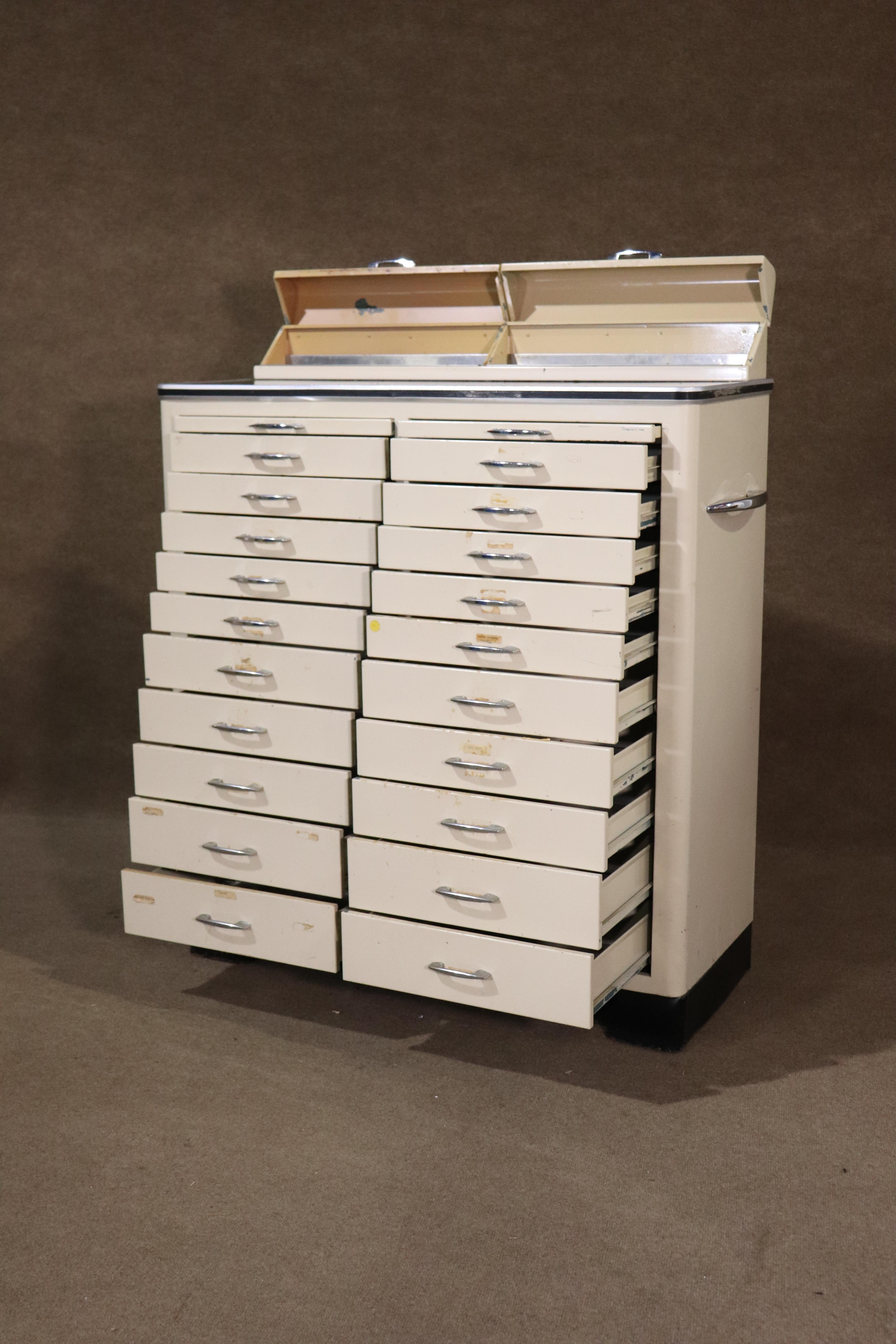 Gabinete dental vintage de metal en estilo Art Déco, ¡con 22 cajones! Pintura blanca con parte superior negra y herrajes cromados pulidos acentuados. 
Por favor, confirme la ubicación NY o NJ