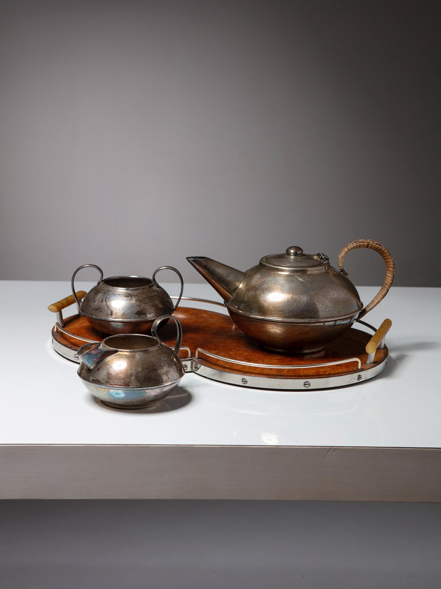 Service à thé fabriqué par Plato. 
Pièces en maillechort électrolytique avec détails en bois et en roseau.
La taille de la théière est en cm 23 x 12 x 16
