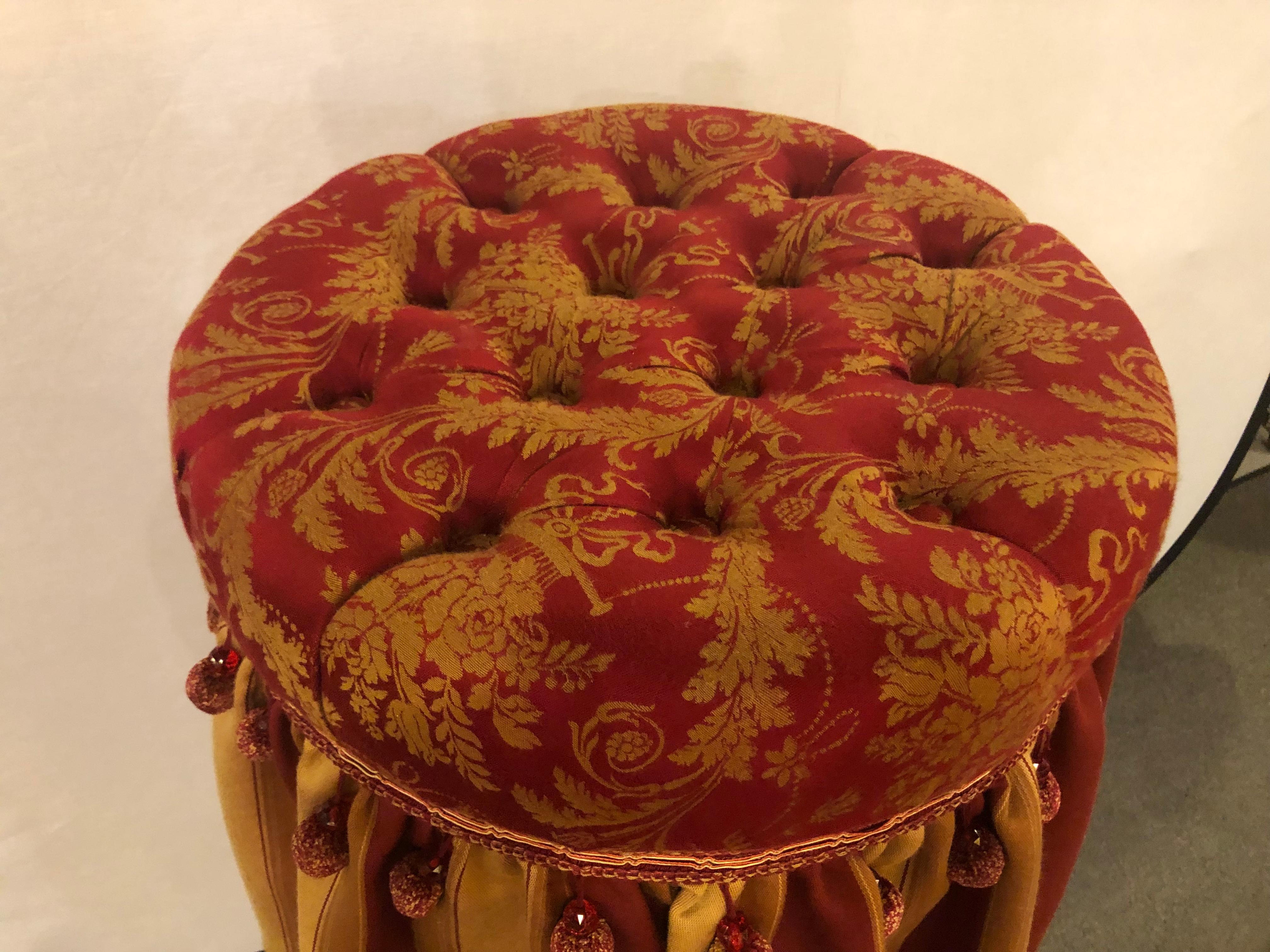 A deco upholstered tufted red and gilt decorated ottoman or footstool. This spectacular footstool or ottoman pouf is simply breathtaking. The finely upholstered piece with a tufted top and decorative base with stripped design and tassel form.