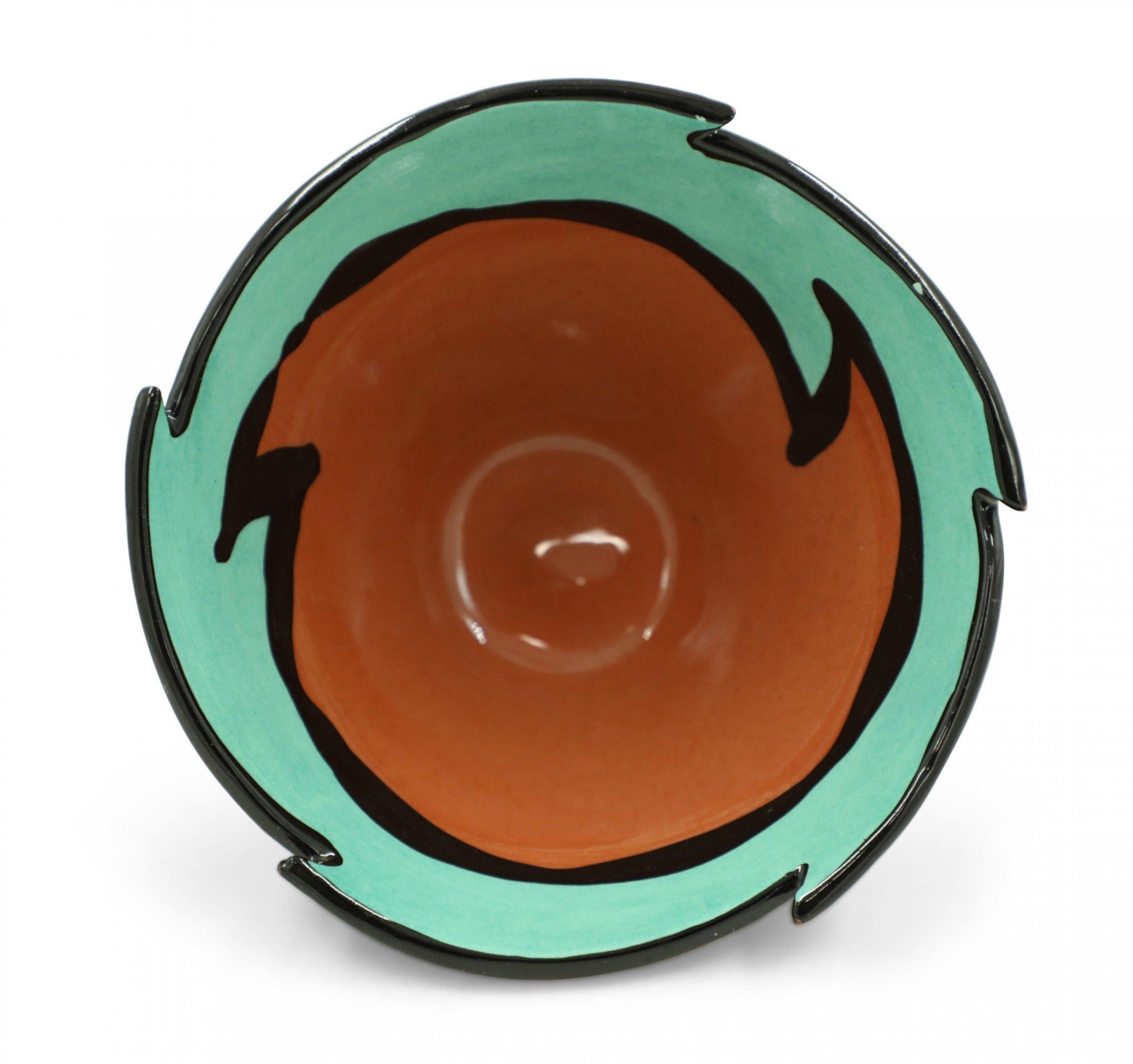 Contemporary decorative ceramic bowl with a wave shaped abstract rim, tapered sides, and a turquoise, terra-cotta, black, and yellow leaf design decorative glaze.
 