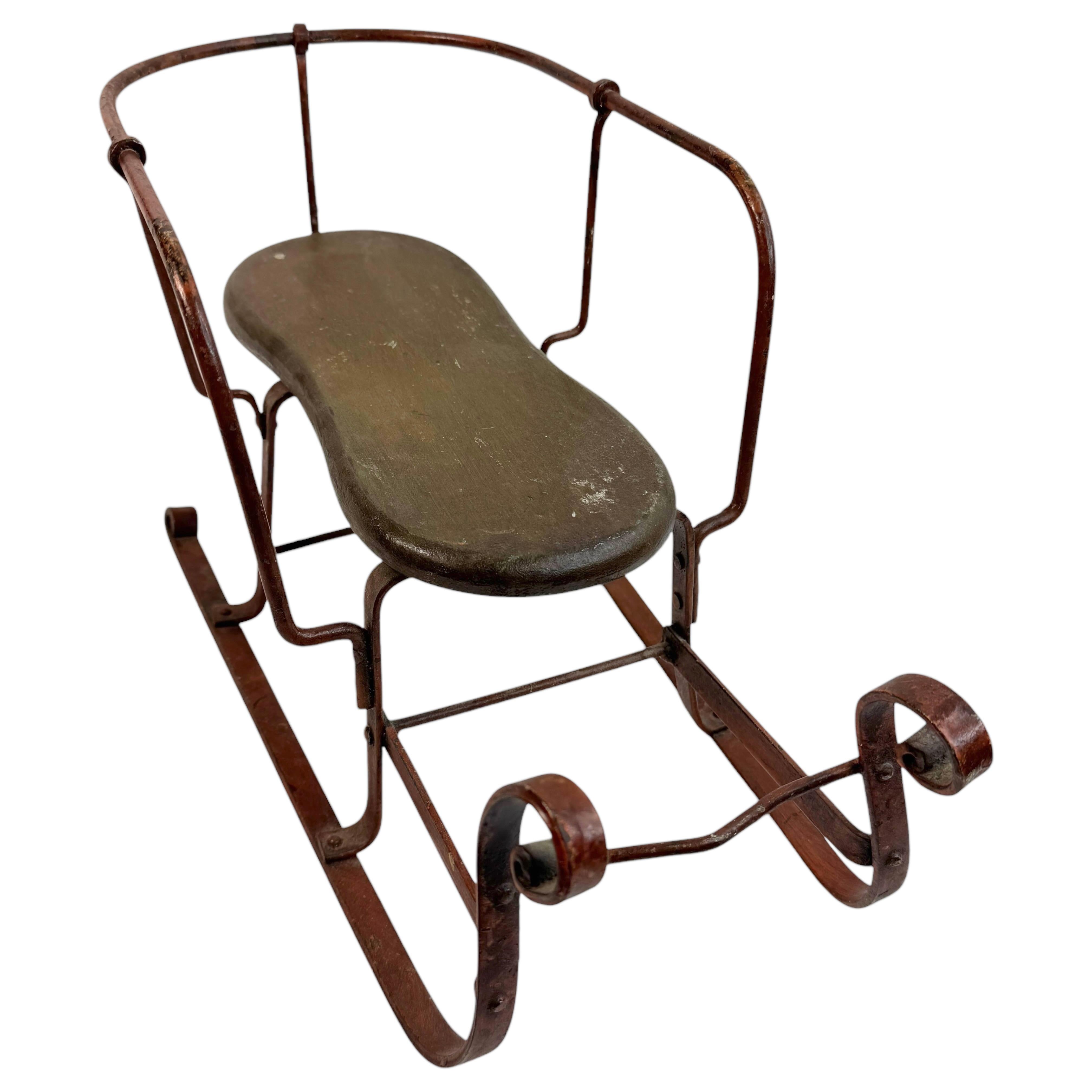 This early 20th century sleigh from Germany is an excellent example of a child's toy or likely a display piece for your doll or teddy bear collection. The piece has a rustic looking seat made of wood and is supported by a frame made of wrought iron.