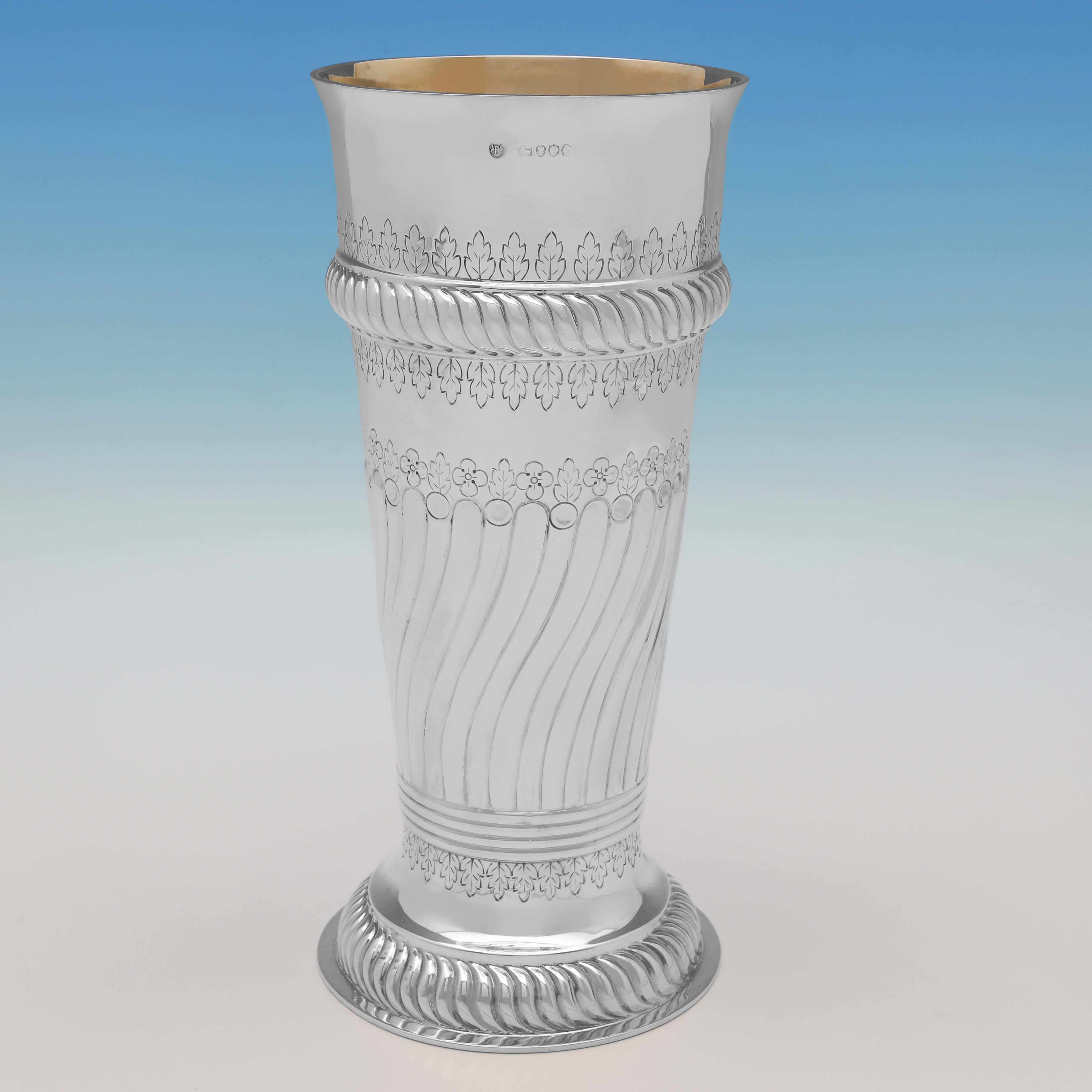 Hallmarked in London in 1889 by Barnards, this attractive, Victorian, Antique Sterling Silver Vase, features chased and engraved decoration, swirled fluting, a vacant cartouche, and a gilt interior. 

The vase measures 10