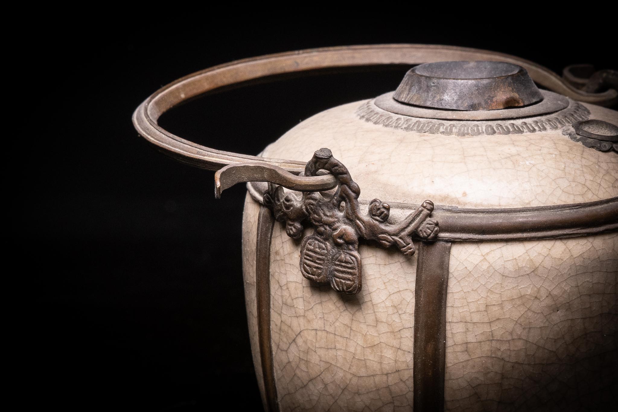 The bowl of the Vietnamese water pipe is jar-shaped. The metal handle allows easy carrying and moving of the object. The pipe stem that is normally places in the water tank, is missing. The craquelure or fine pattern of cracking is intentional and