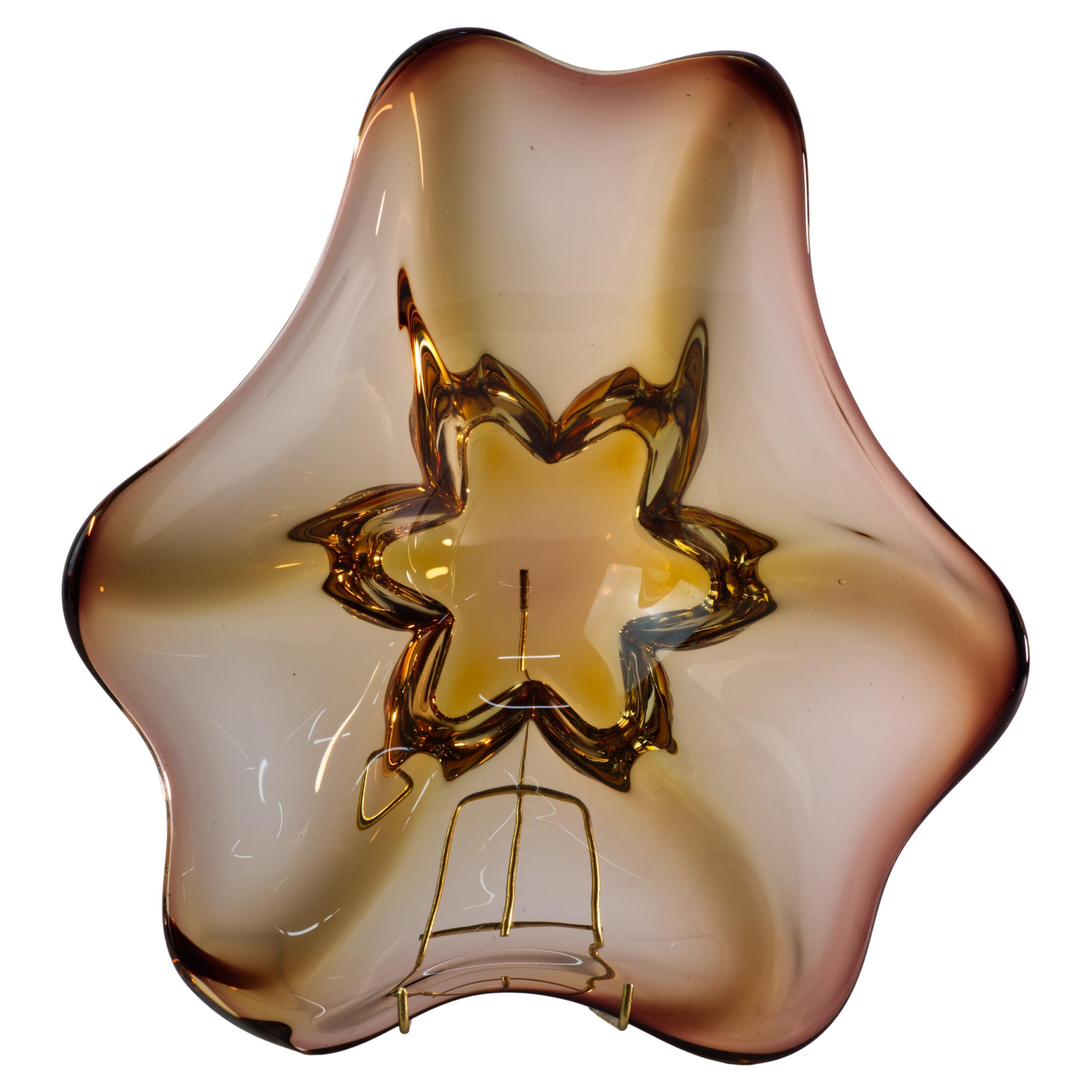  Der bernsteinfarbene Aschenbecher oder die Auffangschale aus Murano-Glas im Vintage-Stil ist mundgeblasen und hat eine organische, frei fließende Form mit asymmetrischen Vorsprüngen am Rand. Die minimale Farbpalette hebt die skulpturale, grafische