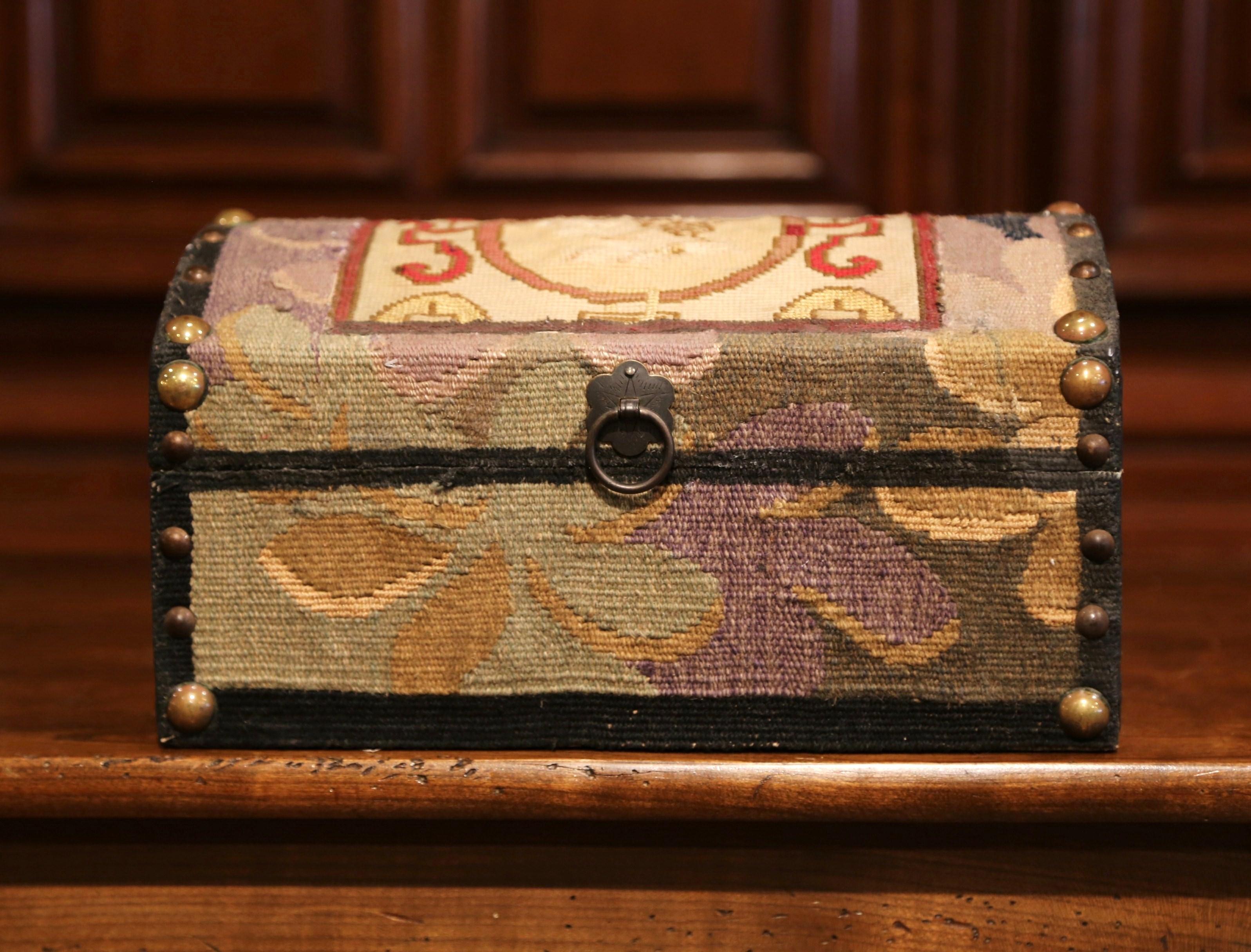 Place this decorative box on a coffee table to store your remote controls, or display it on a shelf. The box with bombe top, is upholstered with antique needlepoint tapestry fragments and embellished with brass nail heads and brass pull. The
