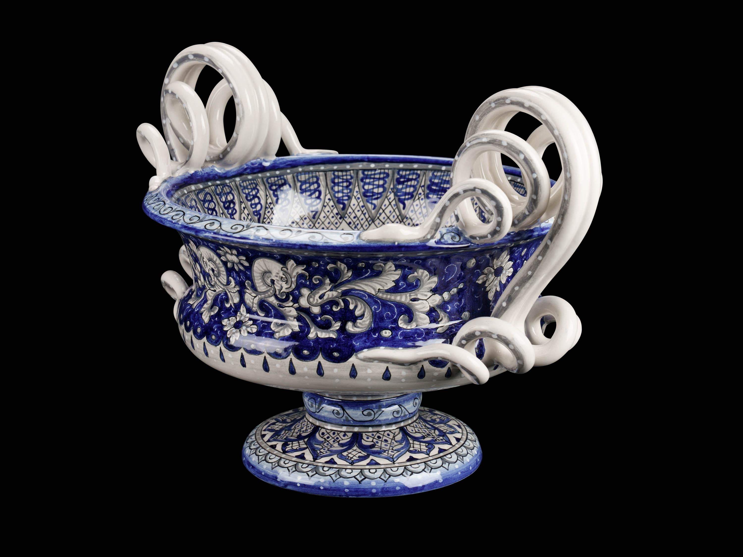 The lavish majolica centerpiece, in the shape of a krater, recalls the ancient structure of the Greek cup that was used to mix water and wine: this beautiful bowl is handmade and hand-painted in Italy, following the original Renaissance painting