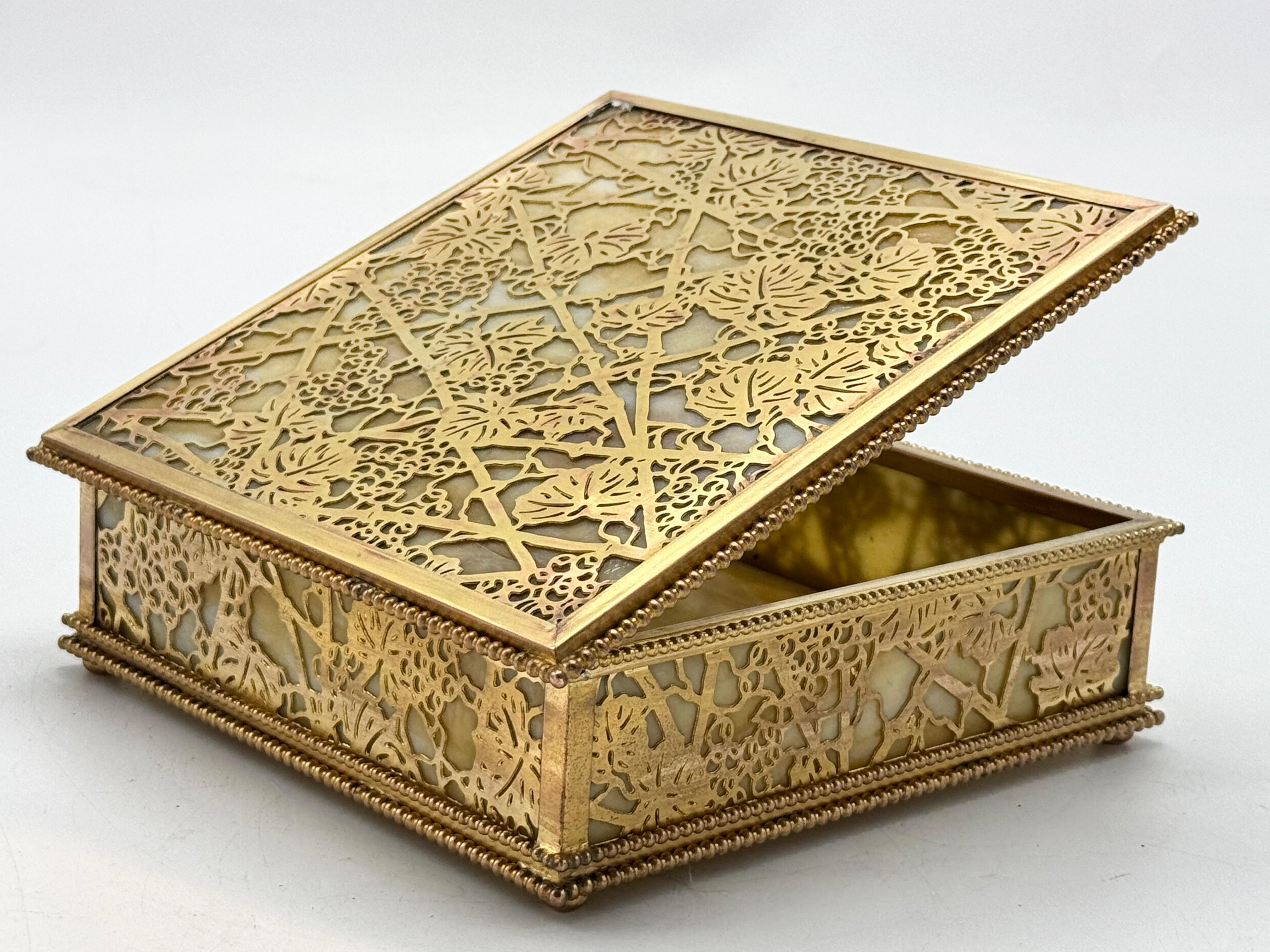 Tiffany Studios New York Decorative Box in Bronze and Slag Glass
This decorative box from Tiffany Studios New York features a square shape with a patinated bronze structure framing slag glass panels. The lid and sides feature an intricate openwork