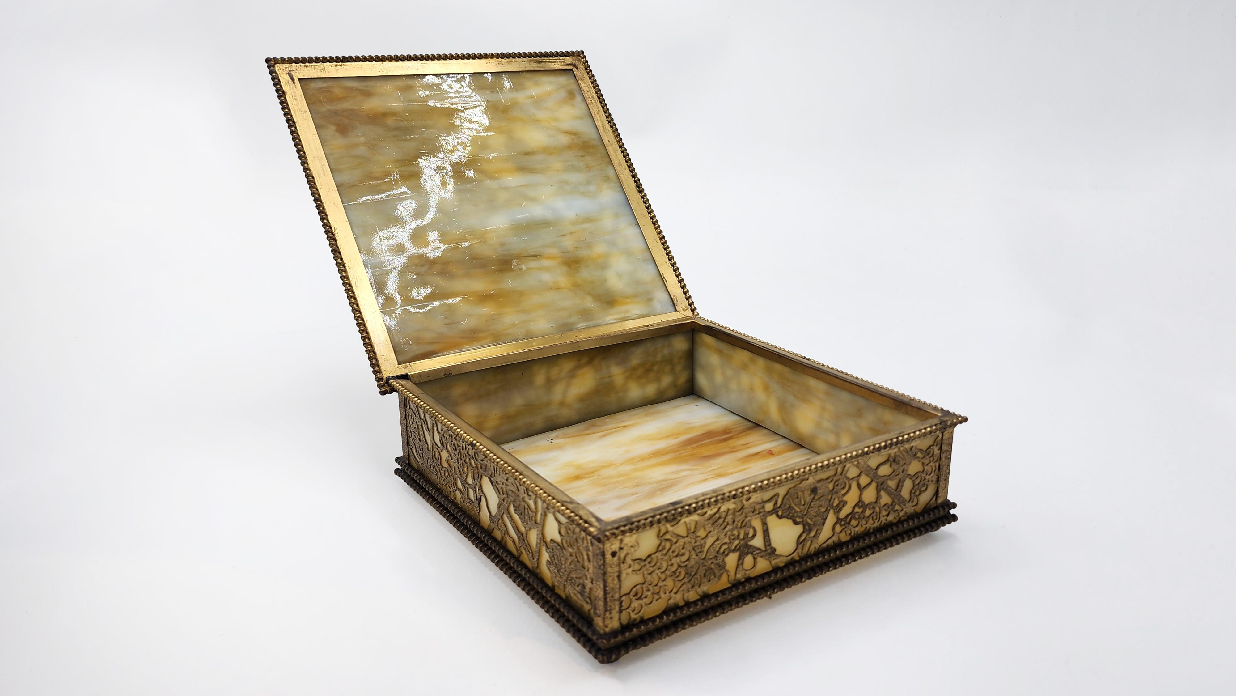 Tiffany Studios New York Decorative Box in Bronze and Slag Glass
This decorative box from Tiffany Studios New York features a square shape with a patinated bronze structure framing slag glass panels. The lid and sides feature an intricate openwork