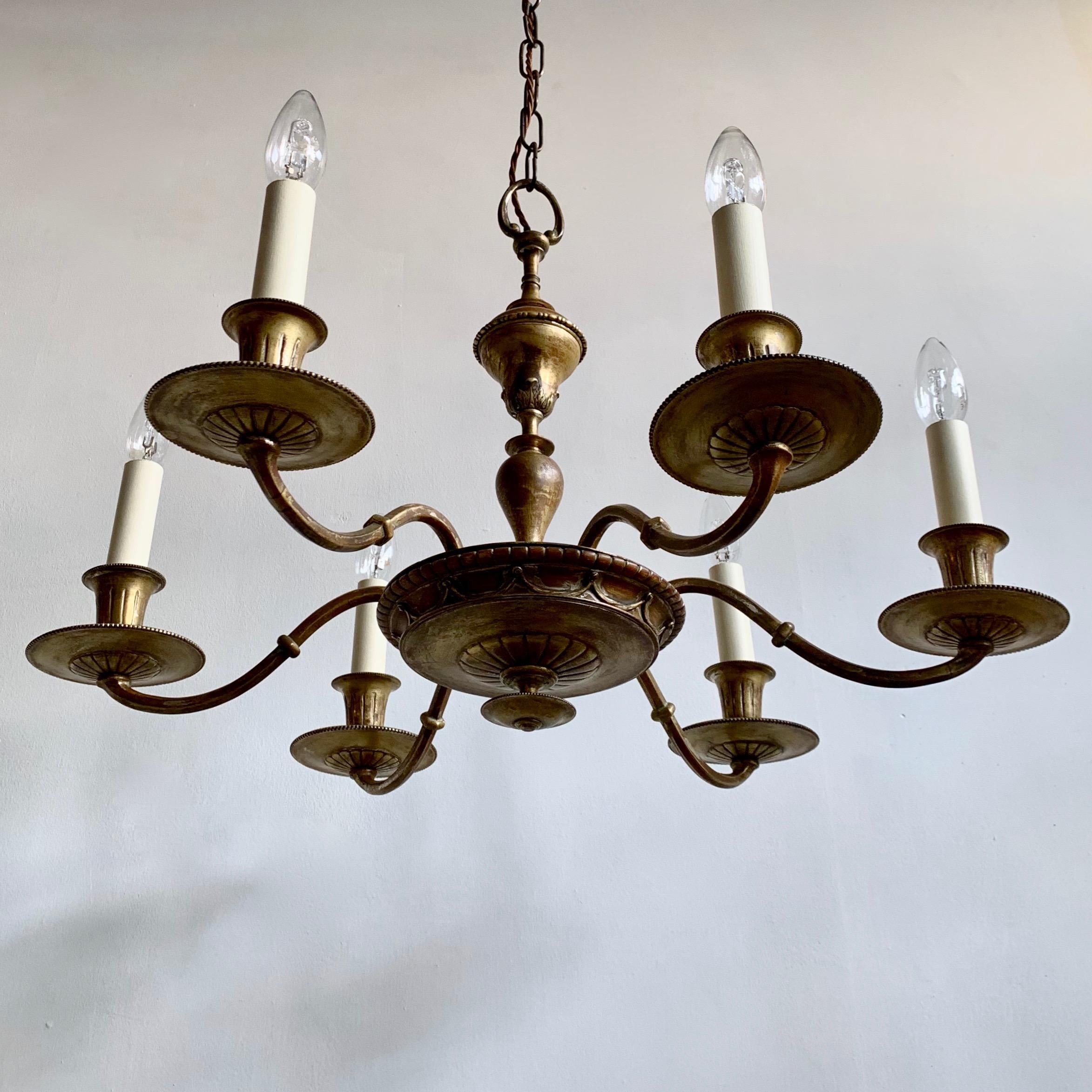 An English Decorative Brass Chandelier with six elegant arms. Converted from a candelabra this gilt brass chandelier dates from late 1800's to early 1900's. It was originally gilt which has worn off in places showing a warm burgundy colour
