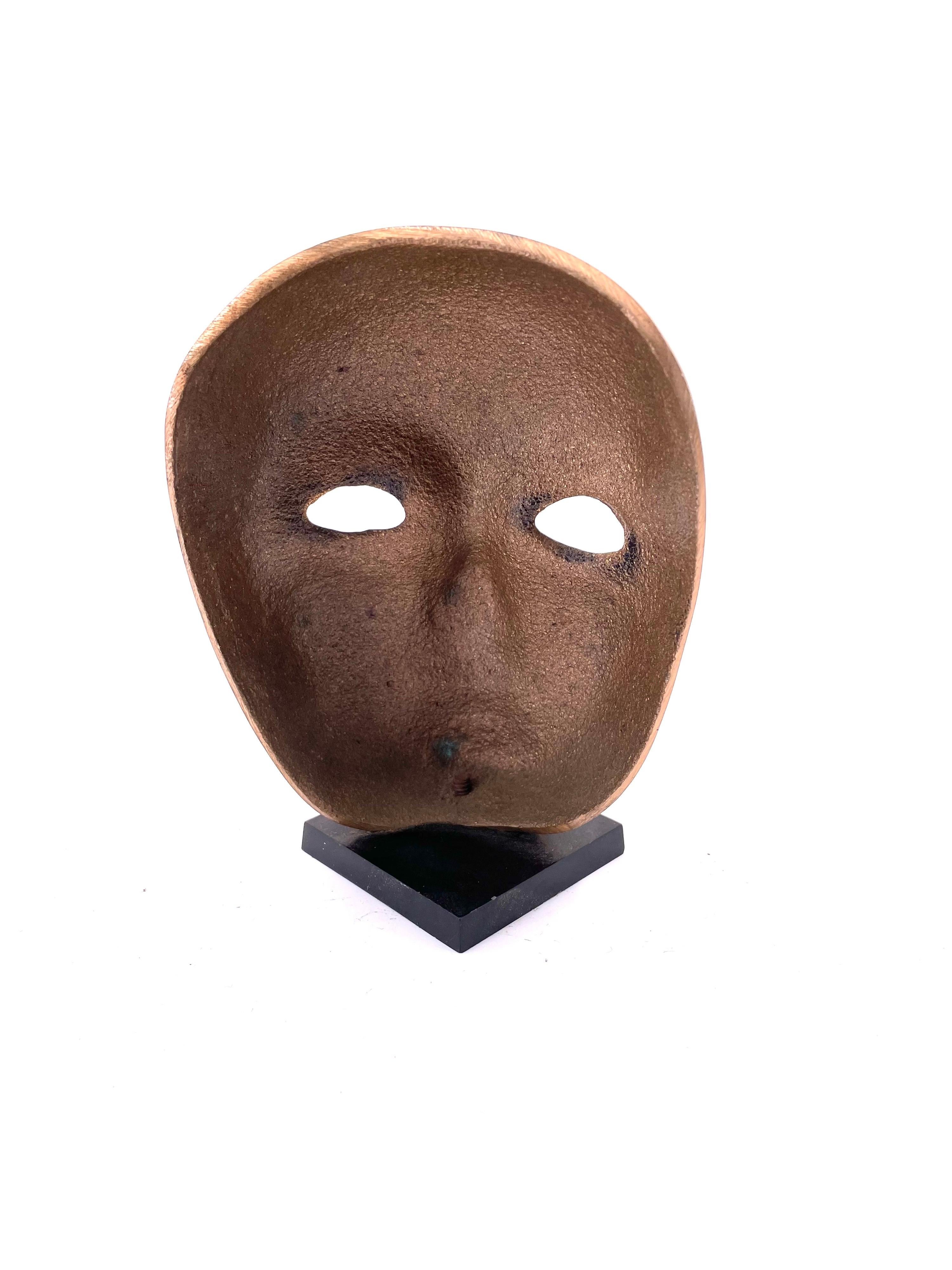 Petite solid polished brass mask sitting on a black lucite base, circa 1980's.