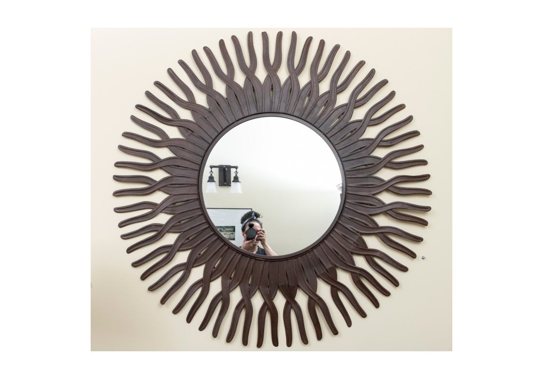 Decorative bronze patinated metal wall mirror with a stylized sun ray form, with over-lapping rays around a flat mirror center.

Dimensions: center mirror - 21 1/4