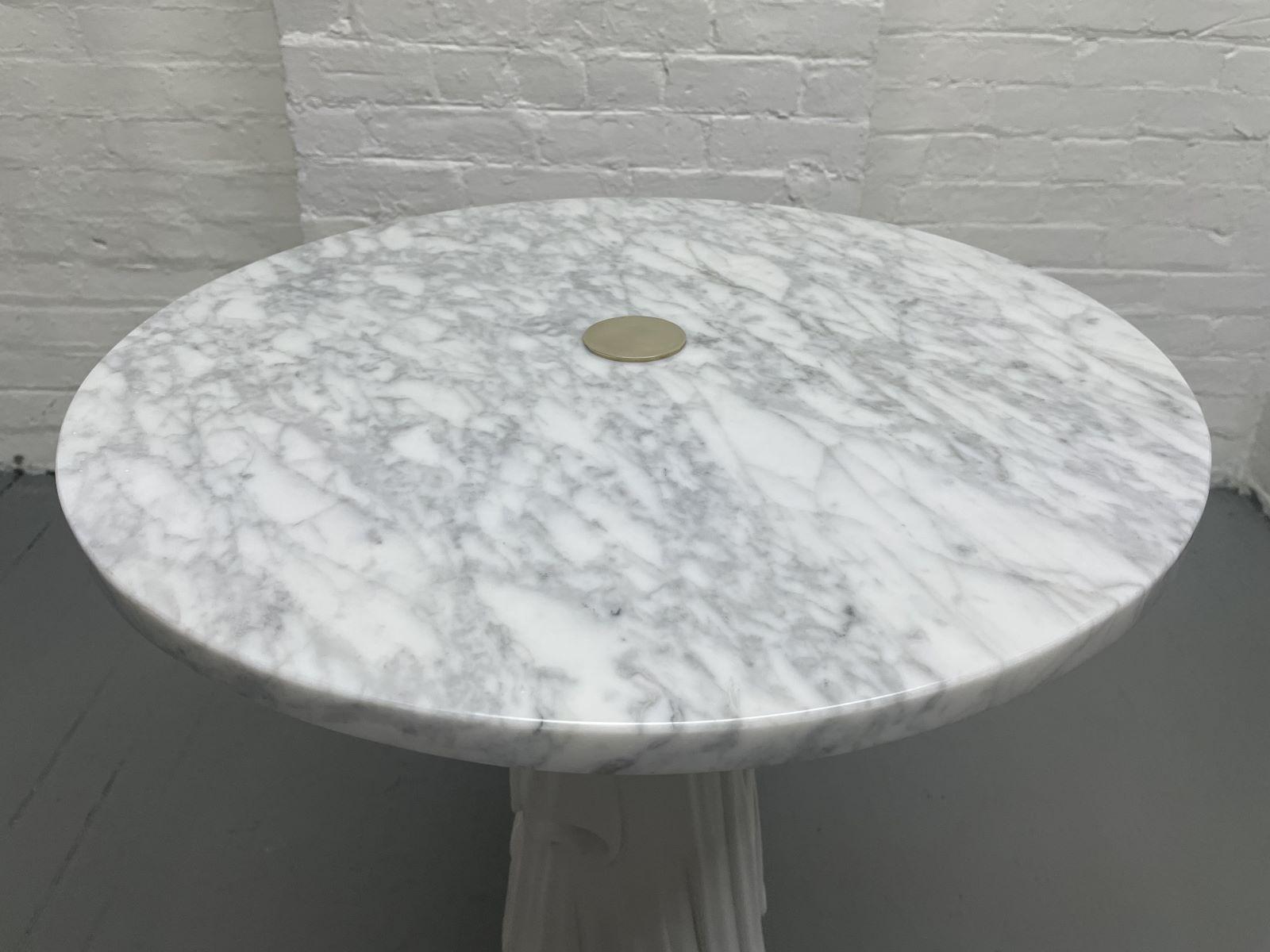 Decorative Carrara marble top Hollywood Regency side table. The table has a painted white solid wood base with a draped pattern. Has a round Carrara marble top with a central brass connector.