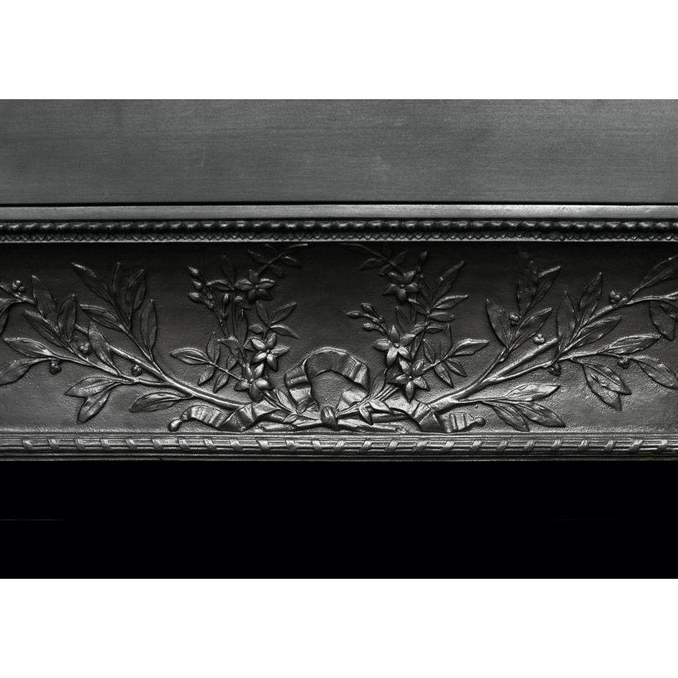 Un interior decorativo de chimenea de hierro fundido contracoeure. Los montantes y la parte superior están decorados con cintas, hojas y flores, con molduras de acanto en el borde exterior y molduras de cuerda en el interior. Se ha ampliado con piso