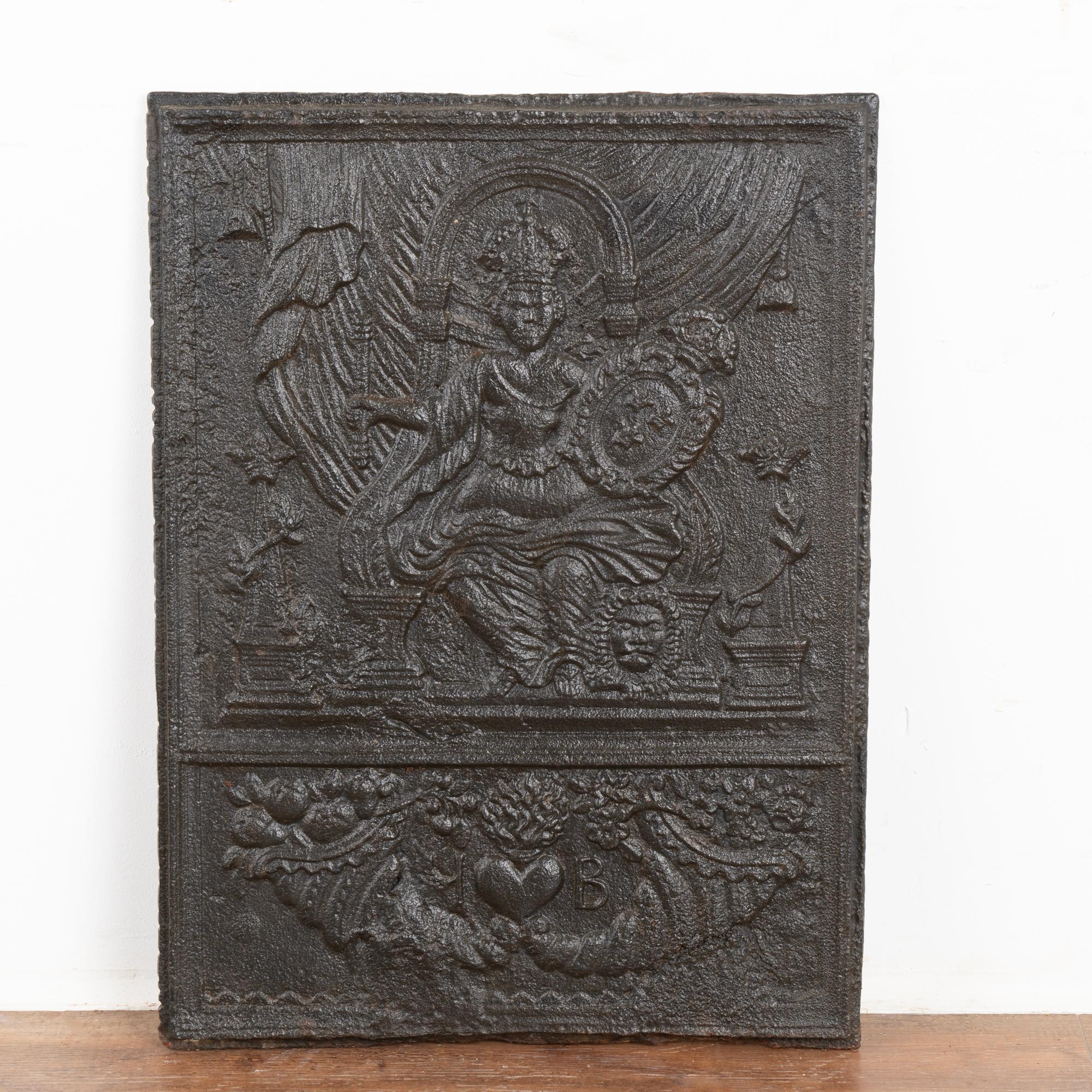 Cast iron fire back with a seated and crowned queen holding a scepter in upper section; in lower section a cornucopia with I B and a heart between the two letters. 
Any scratches, dings, or abrasions are reflective of age and do not detract from