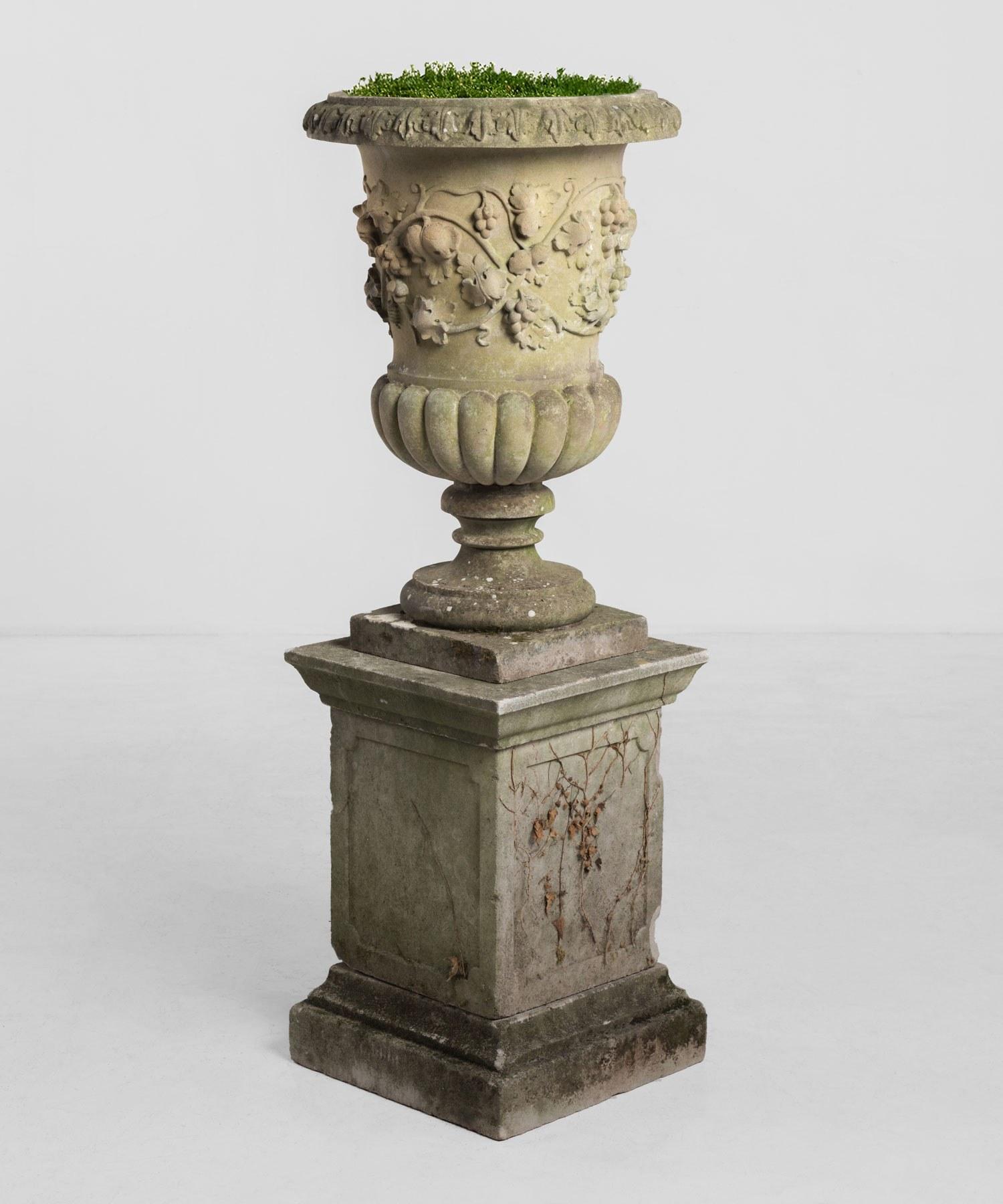 Decorative cast stone urn with pedestal, circa 1950.

Beautifully cast urn with decorative flower motif.