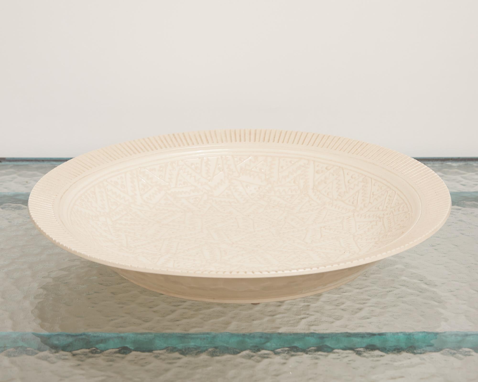 A Roy Hamilton ivory porcelain serving plate. This shallow dish contains a hand painted, detailed triangular pattern in the center. This pattern is made of twisted lines and small dots within each segment. The outer rim is lined with uniform