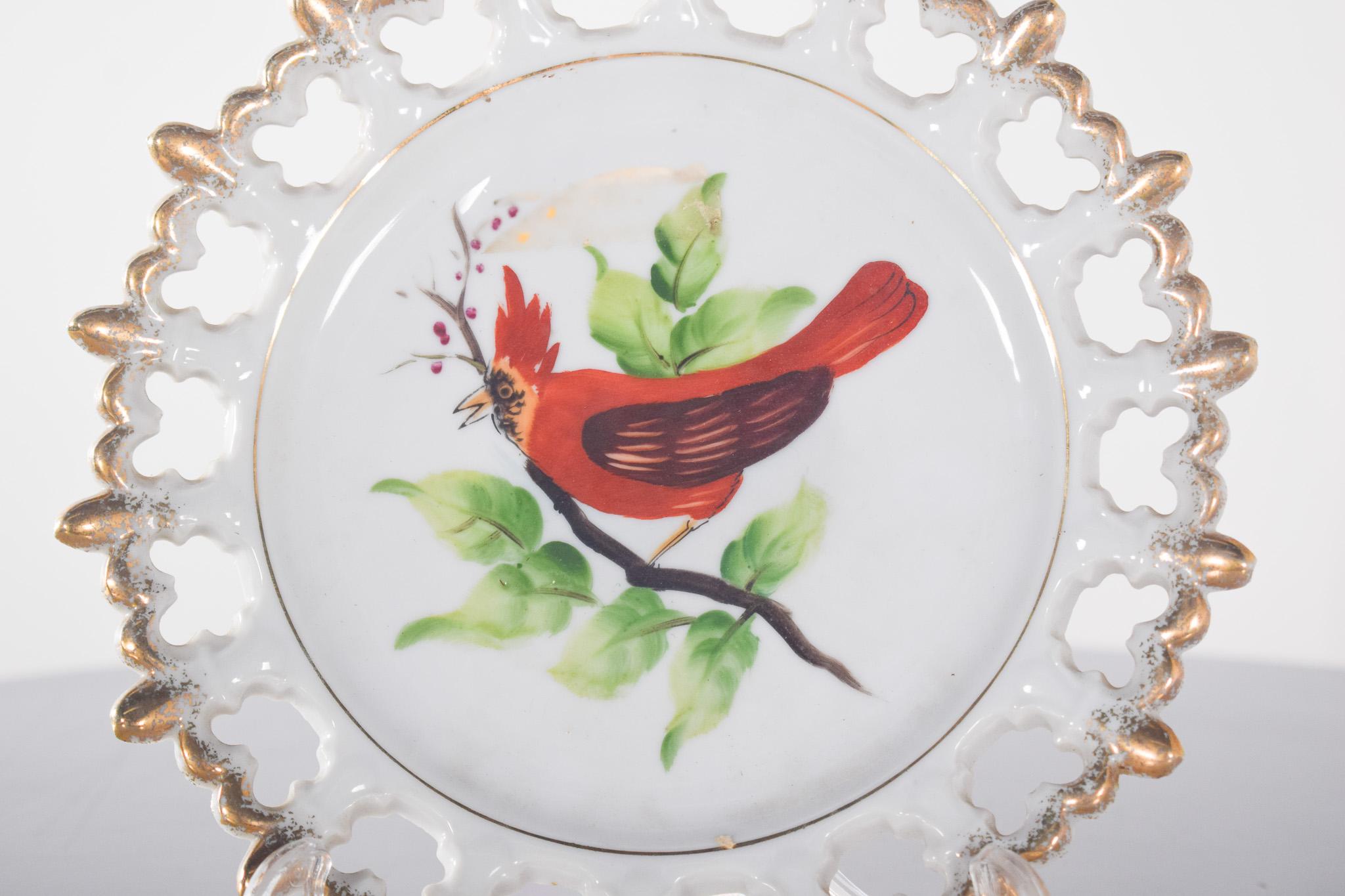 Plat décoratif en céramique. Avec un délicat motif central représentant un oiseau rouge perché sur une branche verte. L'oiseau, probablement un cardinal, est illustré avec des détails exquis dans les plumes et le bec, capturant une scène